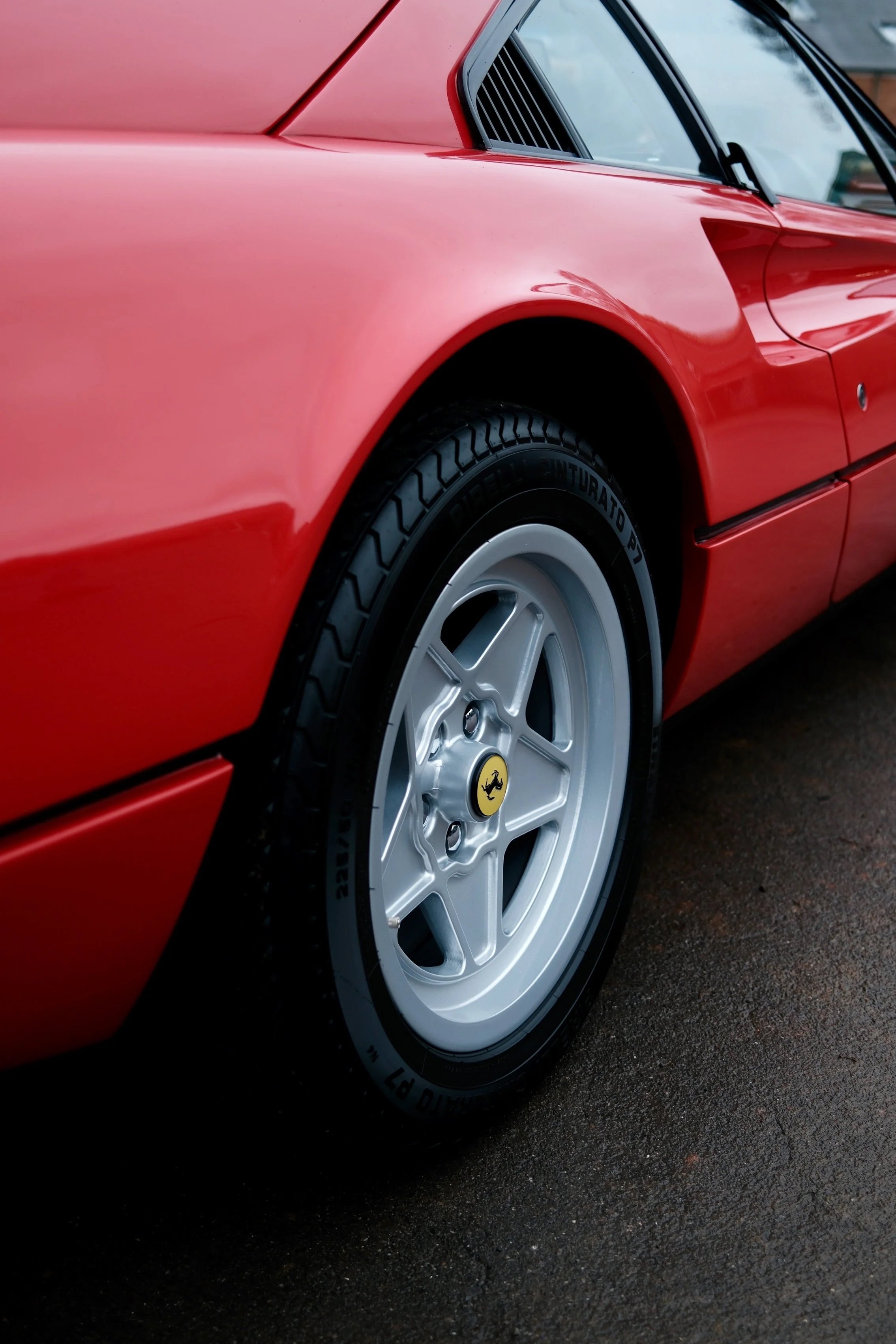 Close-up of a red vintage Ferrari sports car showing the front wheel, part of the door, and side vent.