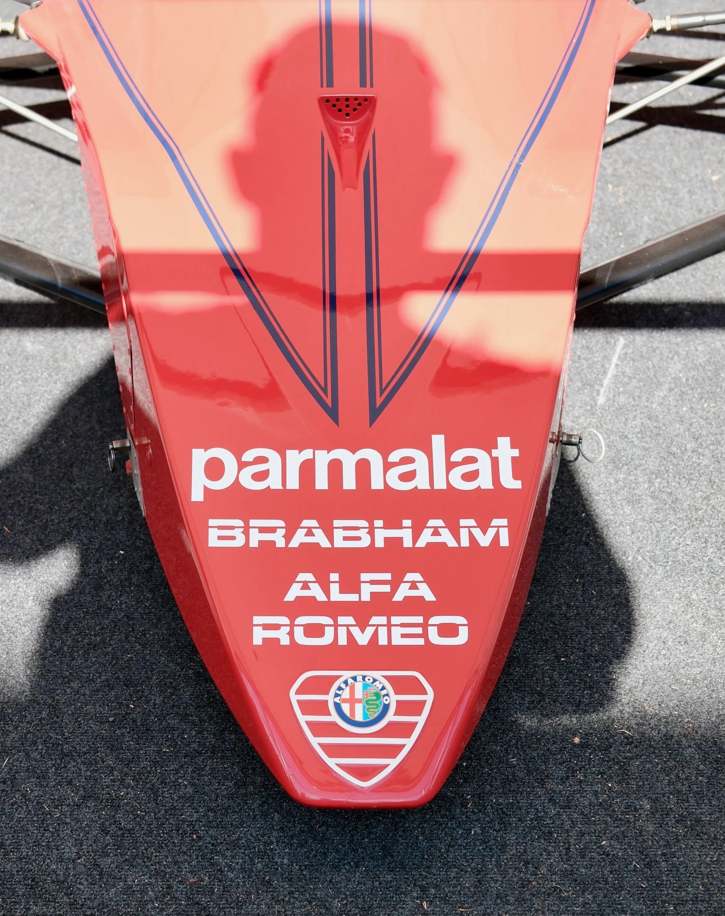 Red triangular sign with the word 'parmalat' and logos of Alfa Romeo and Ferrari, placed on a dark asphalt surface.