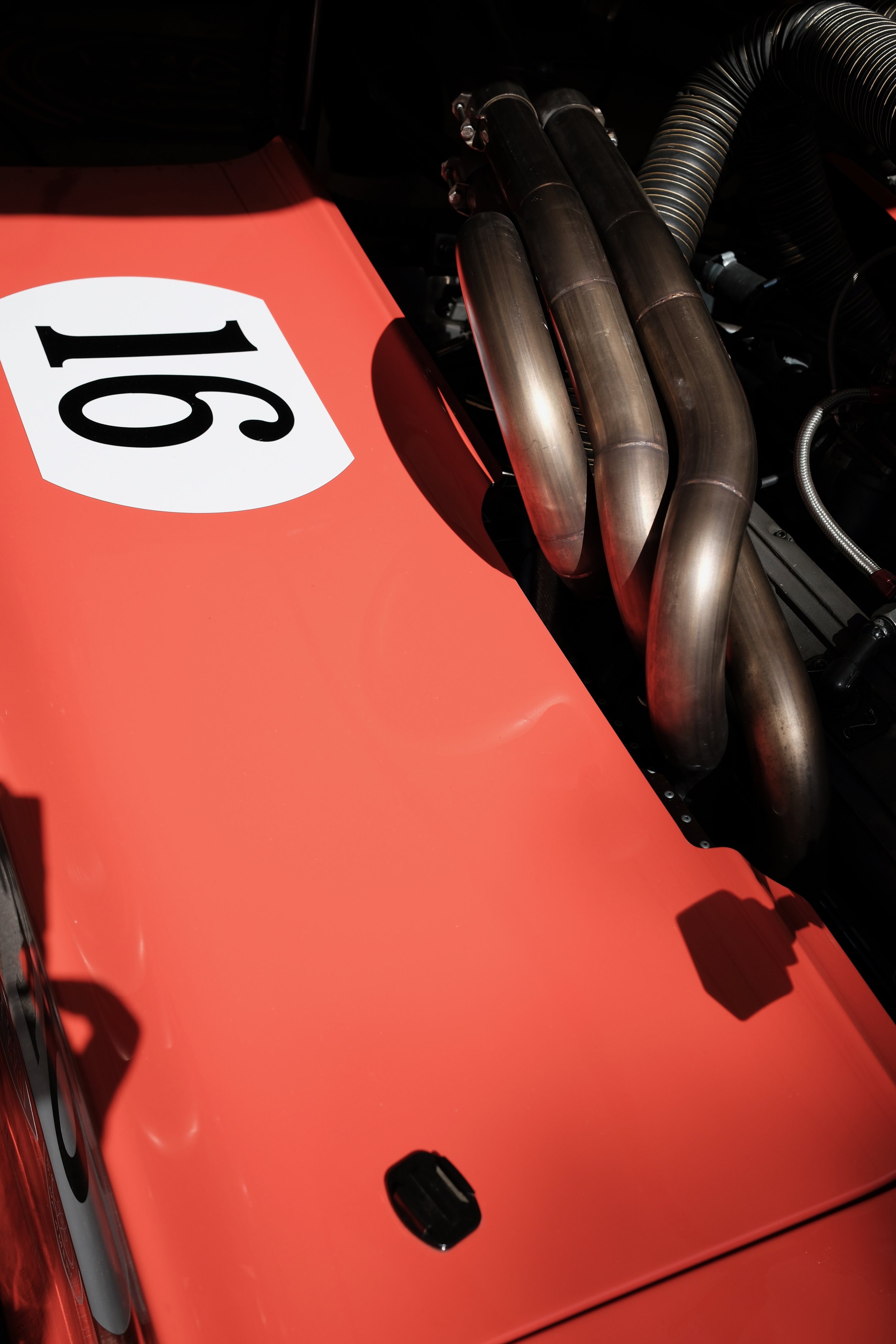 Close-up of a vintage racing car with a bright orange body, showing exhaust pipes and a number 61 decal.