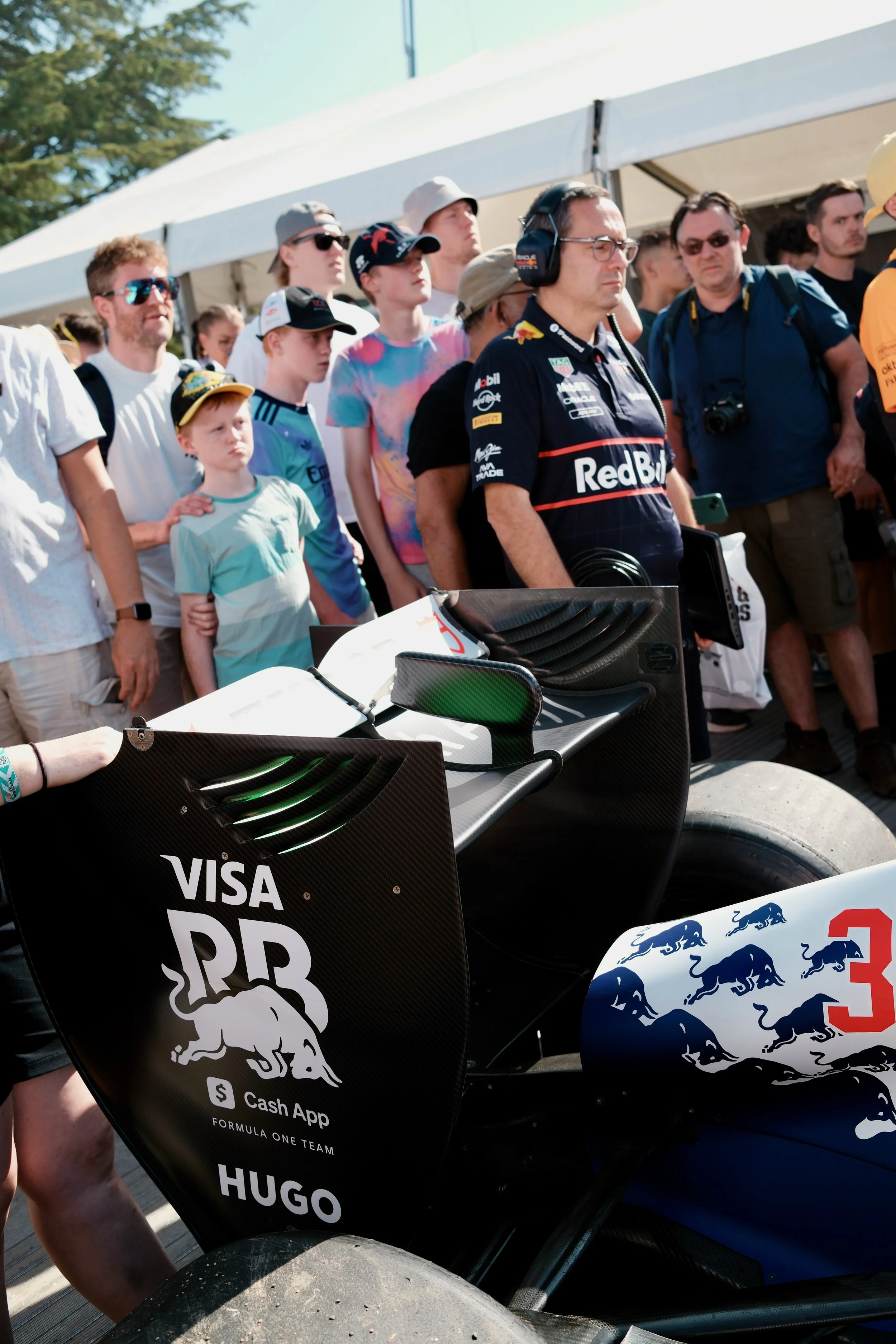 Race car with logos of Red Bull Racing and sponsors, including Visa and Puma, and a crowd of spectators behind a white canopy at a racing event.