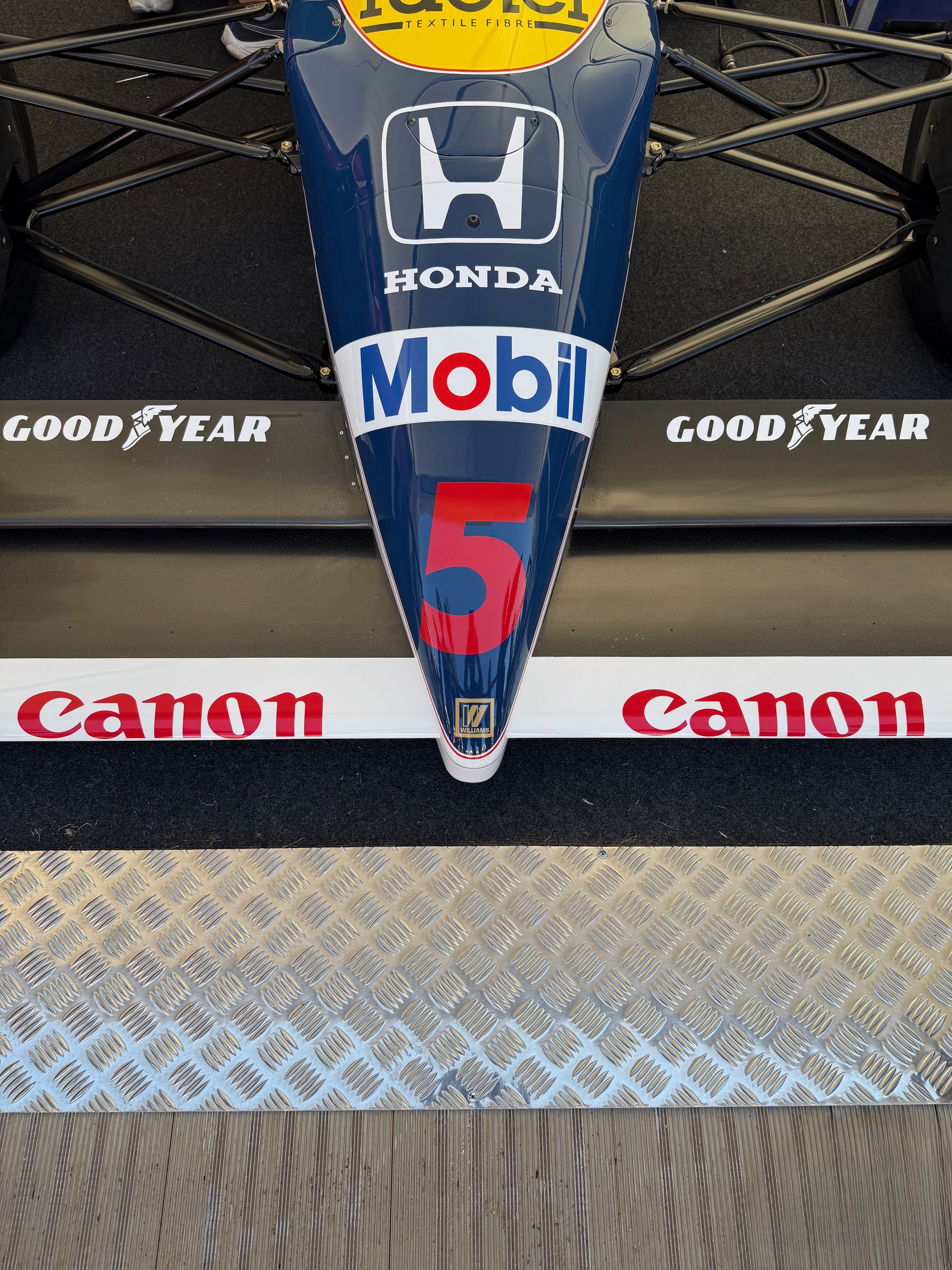 Top view of a Williams Formula 1 car with sponsors, including Honda, Mobil, and Canon, on a metal walkway with a textured, ribbed surface.