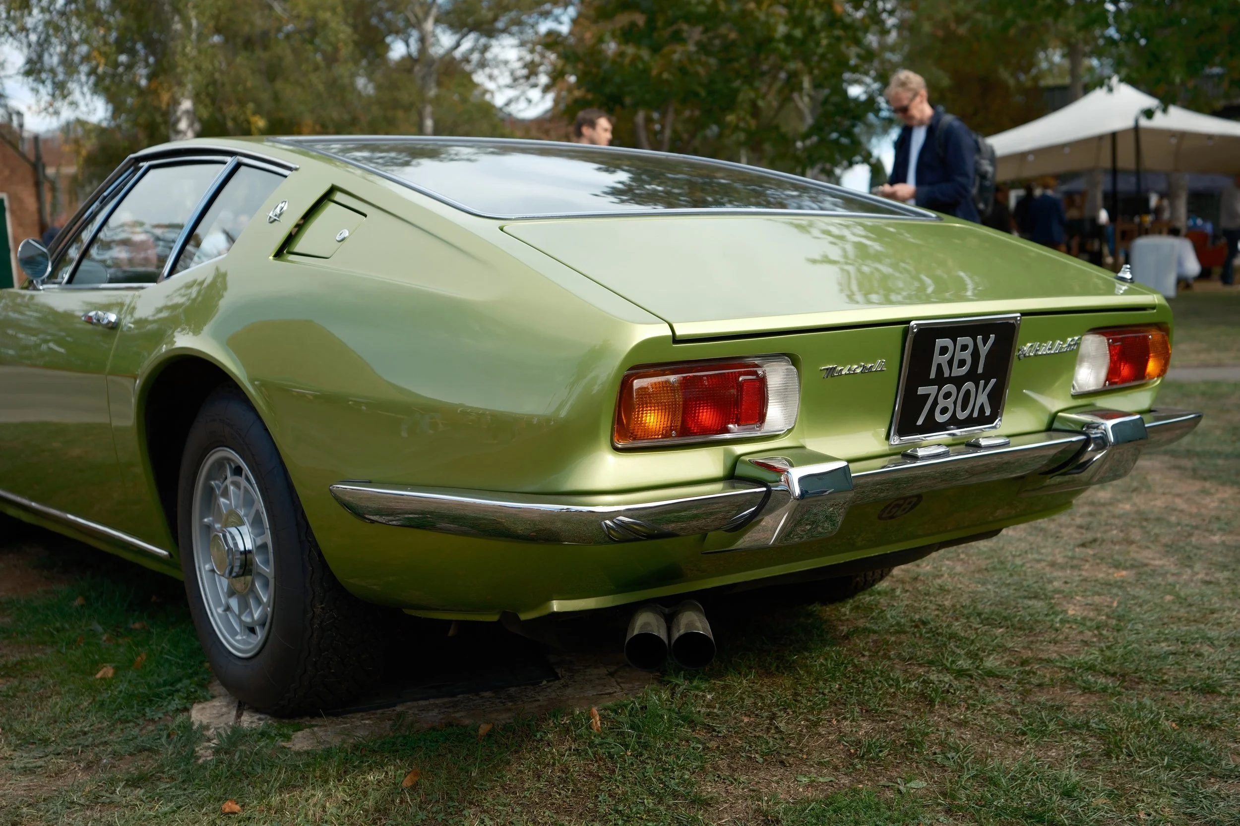 A vintage lime green Maserati Ghibli car on grass at a car show with people and trees in the background.