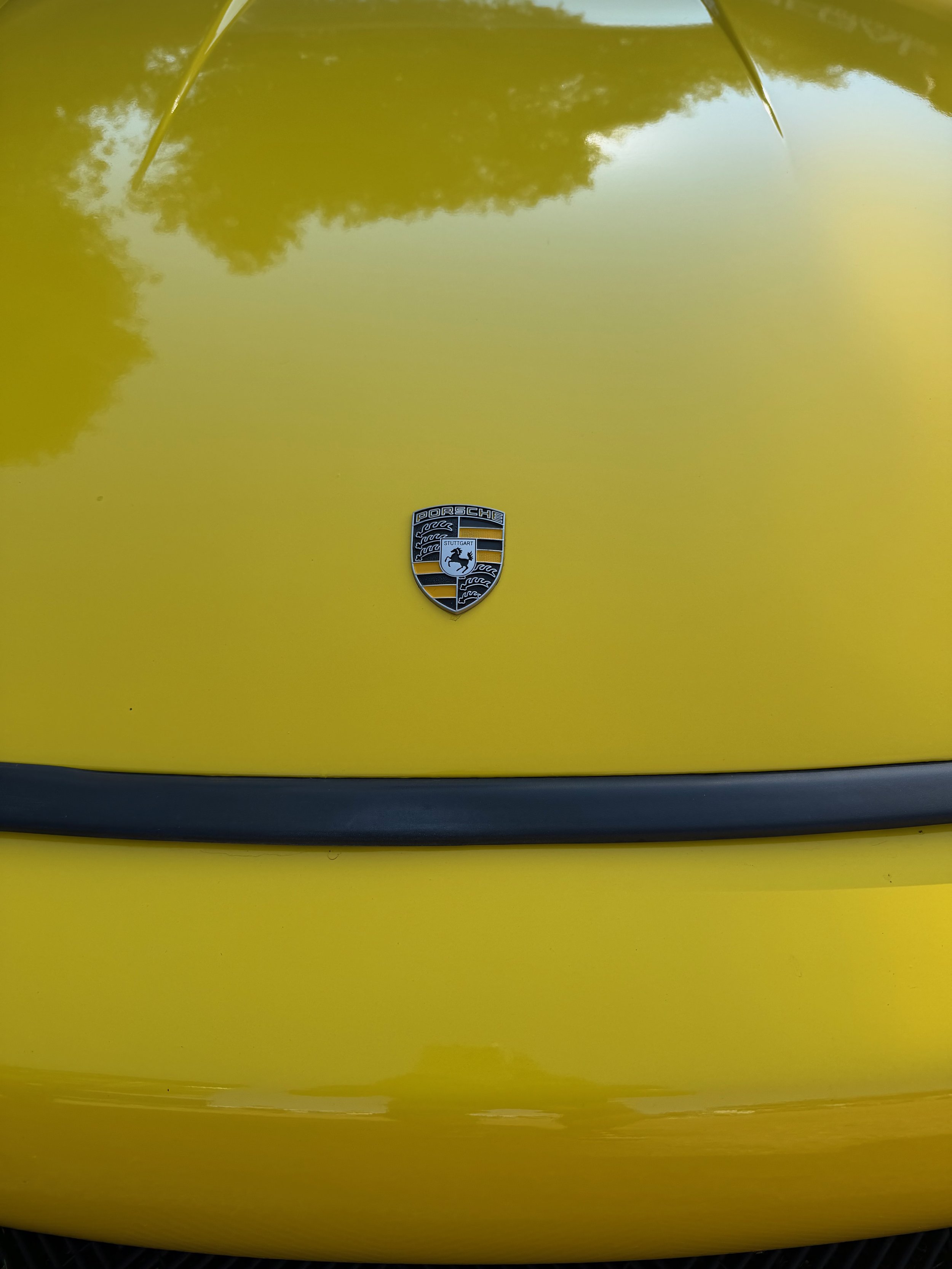 Close-up of the hood of a yellow Porsche car, featuring the Porsche emblem in the center.