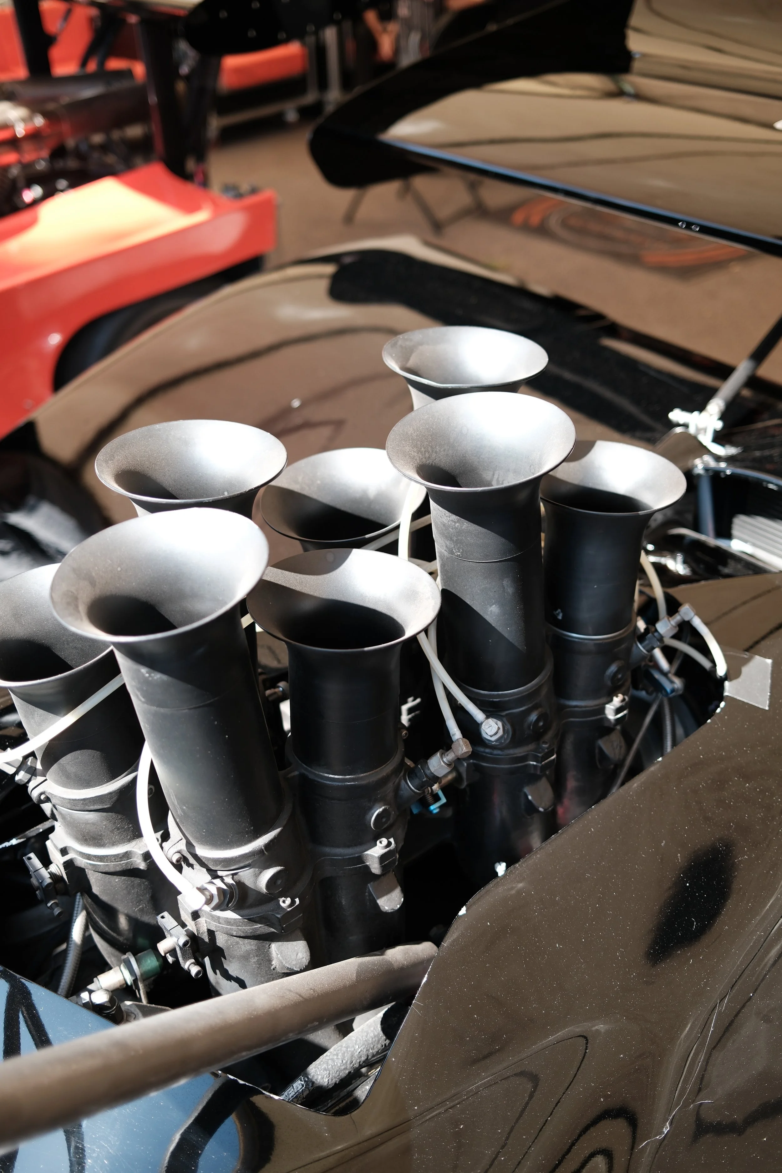 Close-up of an engine with black intake tubes and metallic exhaust tips on a motorcycle, with a blurred background of an orange and black surface.
