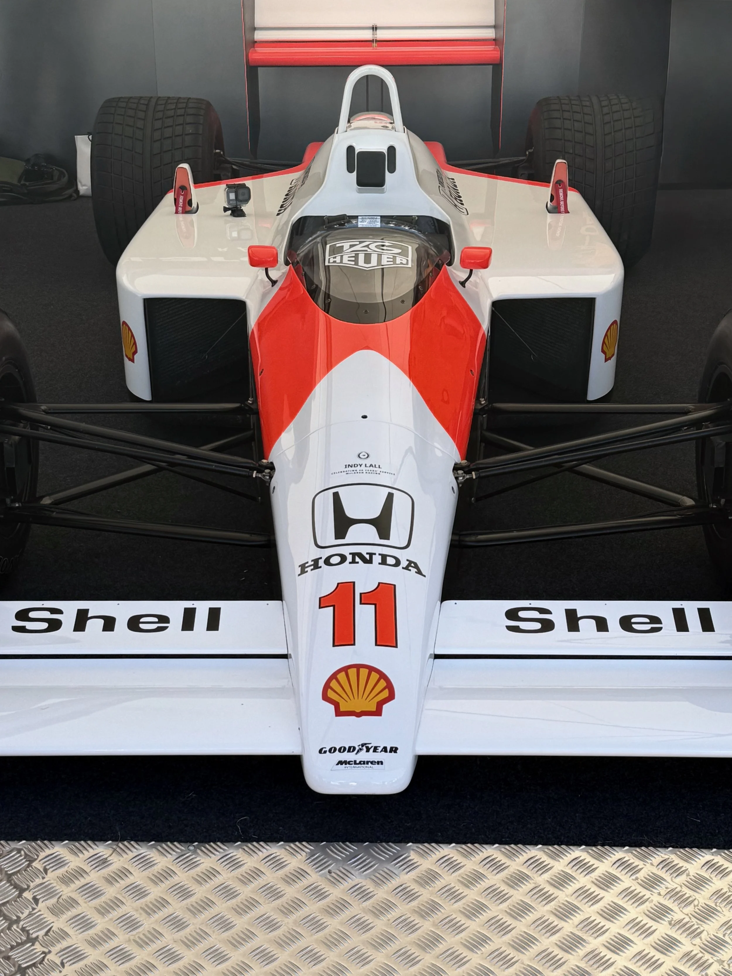 A vintage race car with sponsorship decals, featuring a white body with red accents, the number 11 on the front, and logos including Honda, Shell, Shell, Goodyear, and McLaren. The car is positioned on a metallic patterned surface.