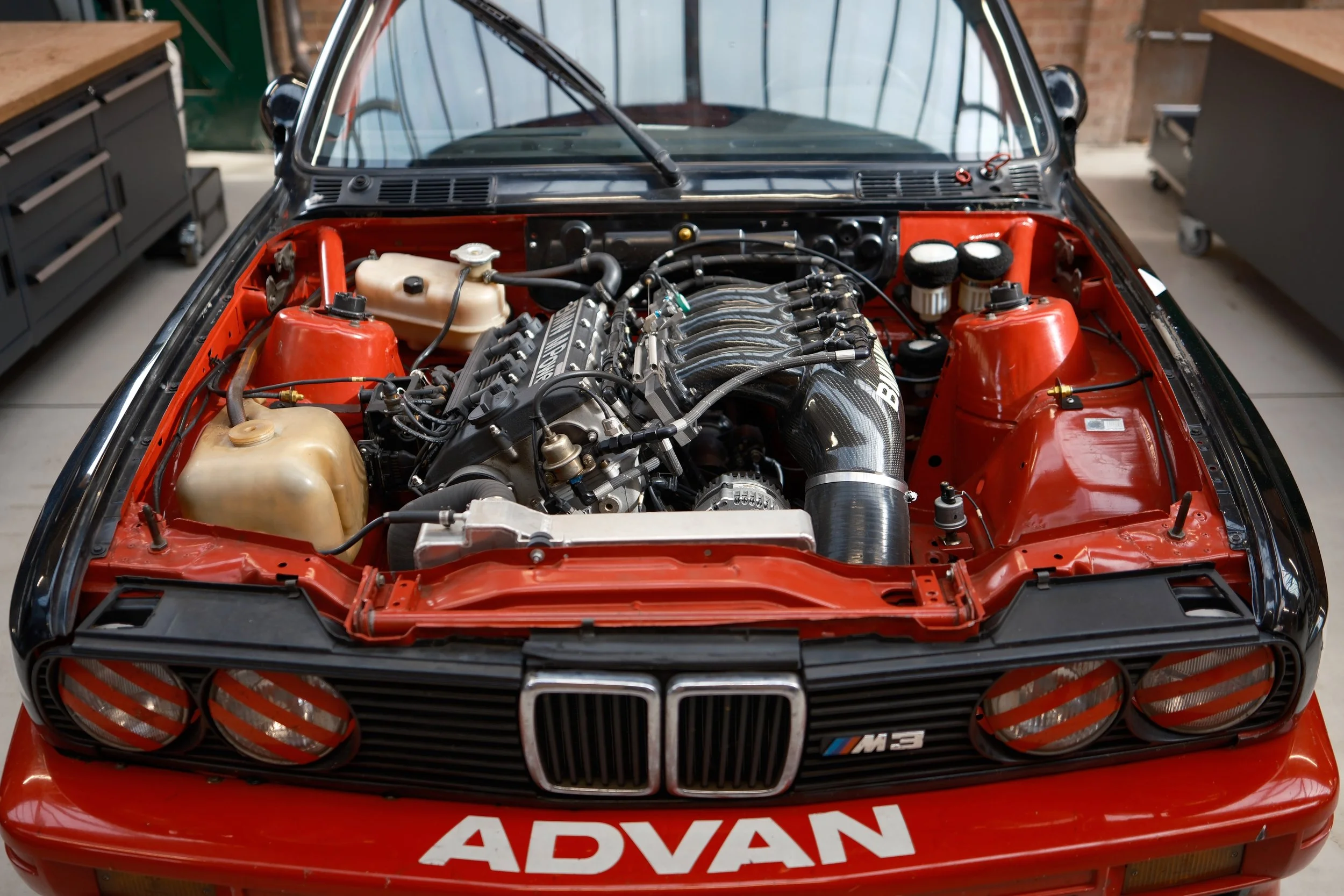 Close-up of a BMW car engine in a red engine bay, showing various engine components, tubes, and wires.