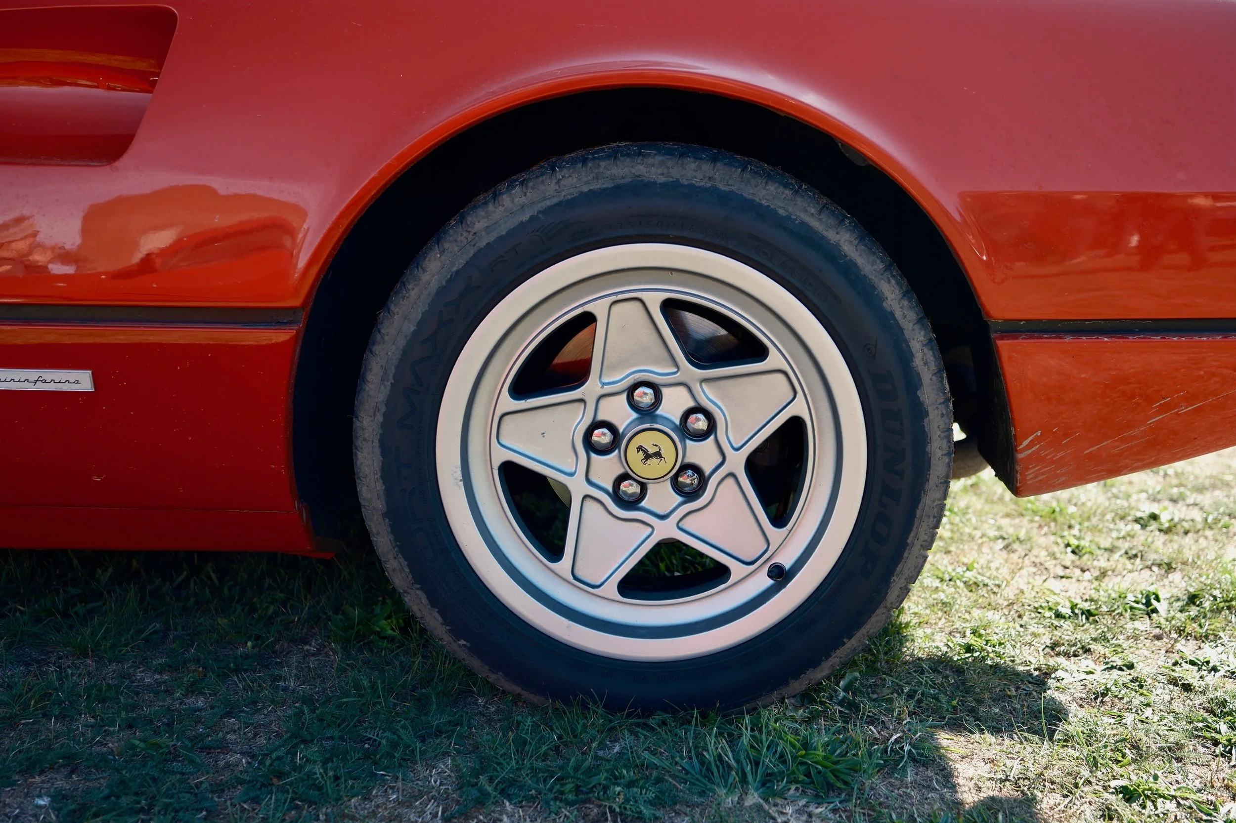 Close-up of a red sports car's front wheel with a white rim and a yellow Ferrari logo at center, parked on grass.