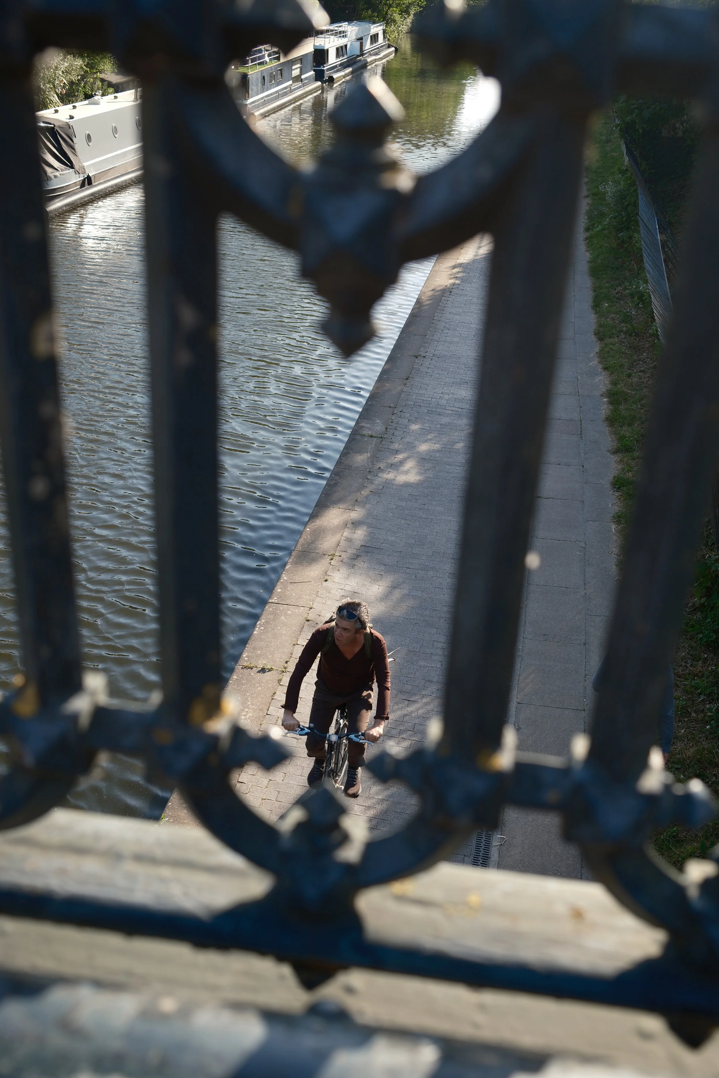 A person riding a bicycle on a sidewalk next to a canal, seen through a decorative iron fence.