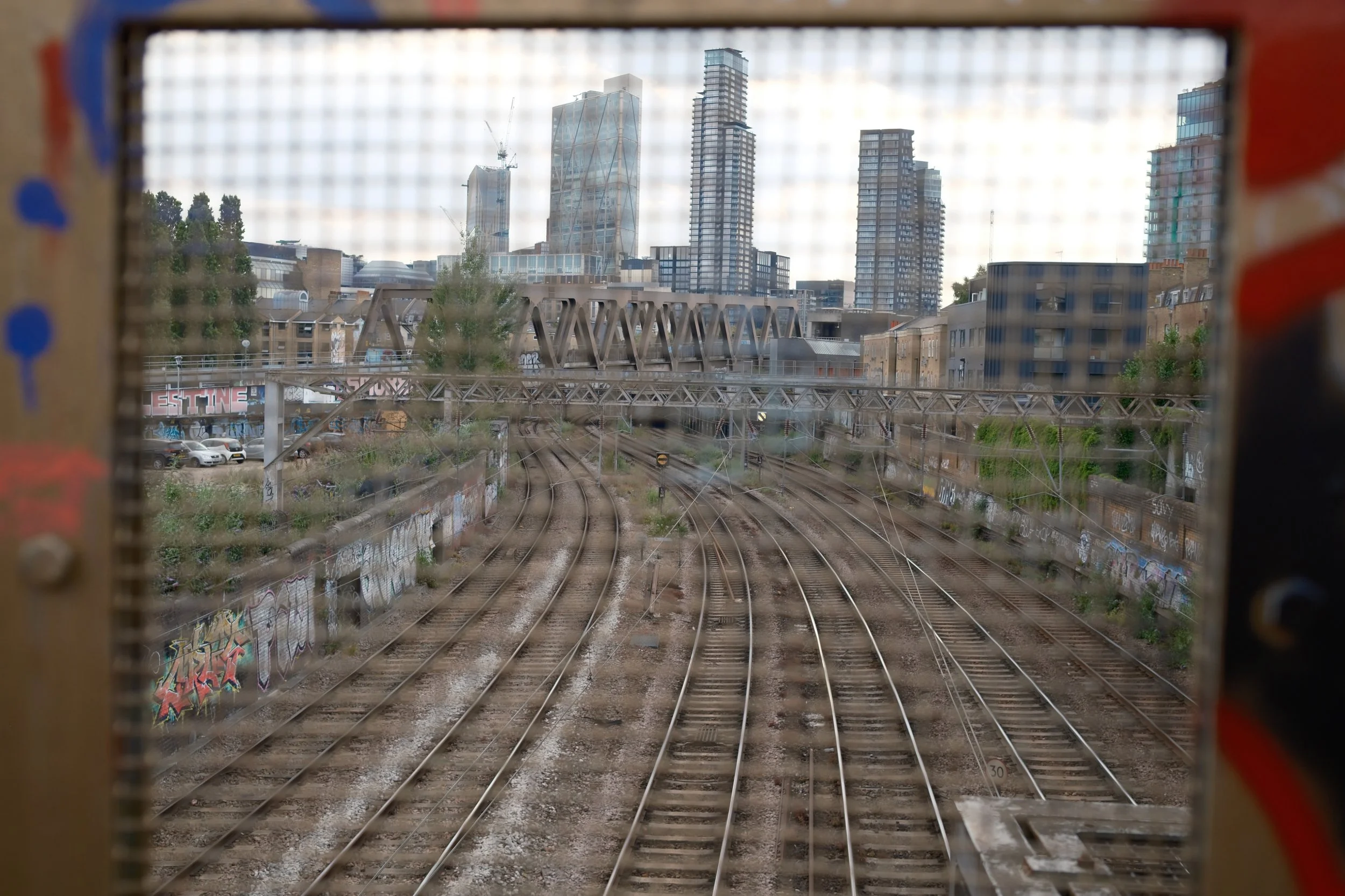 View of city skyline with tall modern buildings, viewed through a structure with railroad tracks in the foreground.