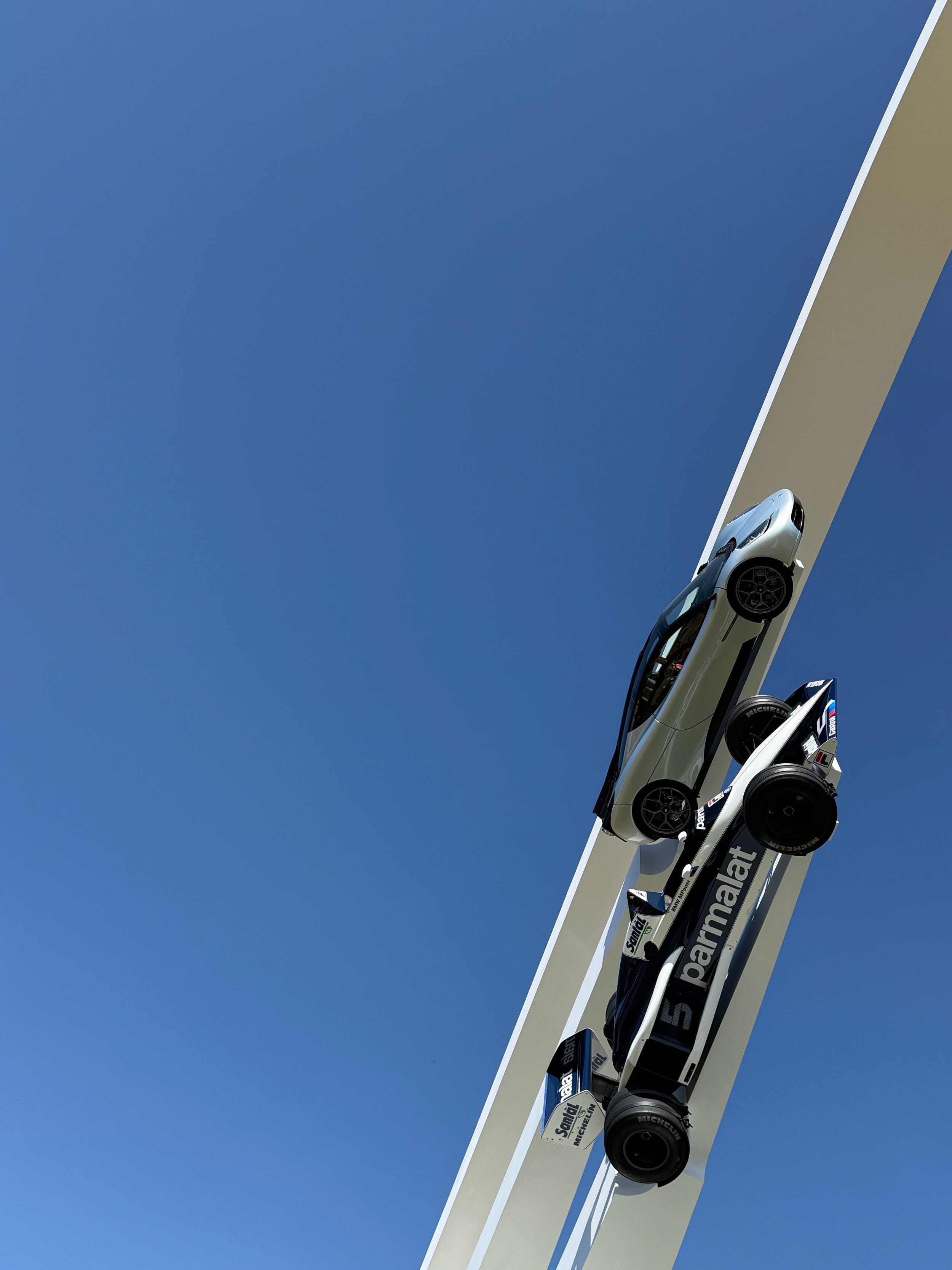 A series of racing cars mounted on a tall, angled display structure against a clear blue sky.
