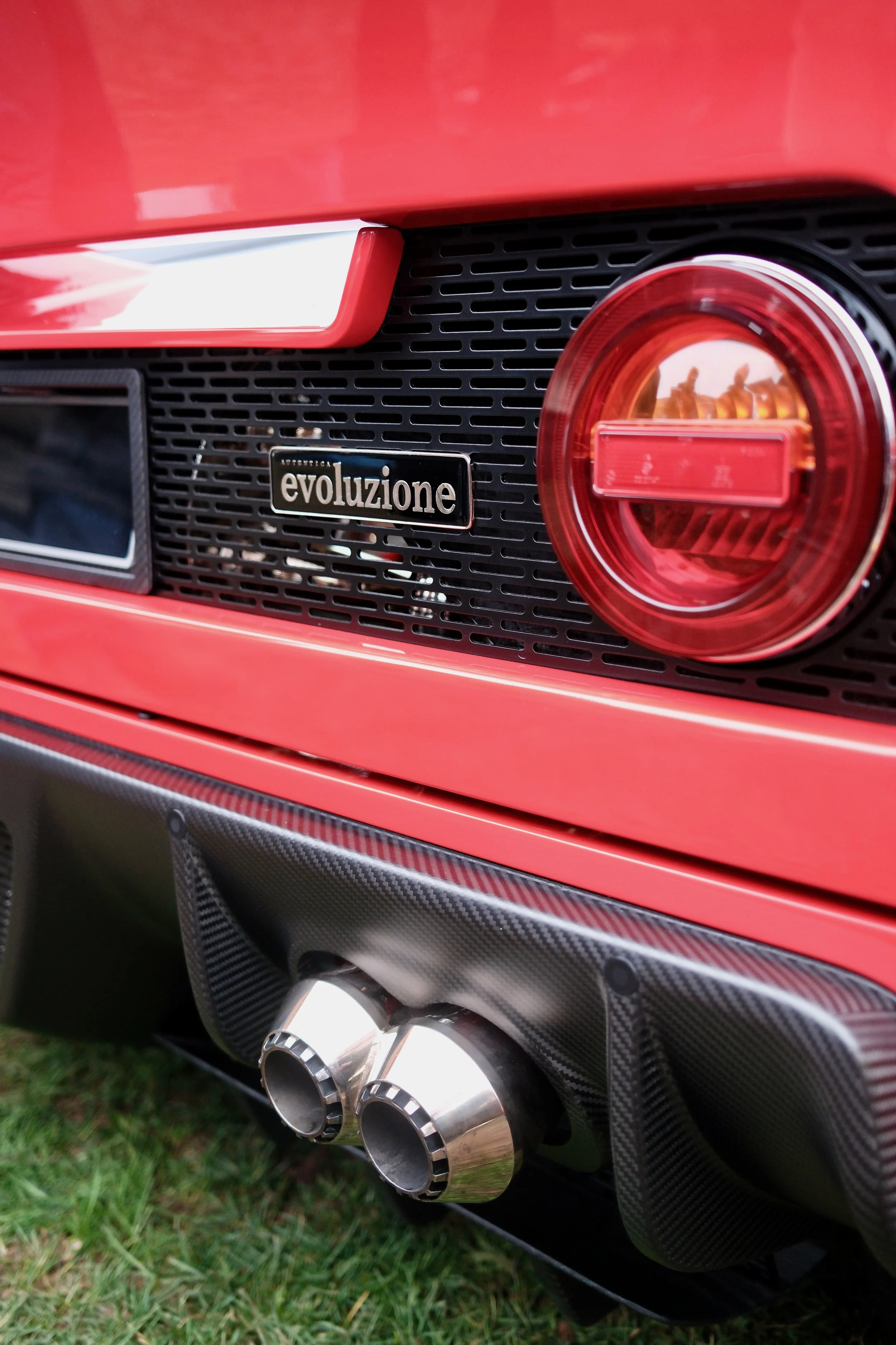 Close-up of the rear of a red Ferrari with a black grille, a Ferrari badge that says 'evoluzione', and a dual exhaust pipe system with shiny metallic tips.