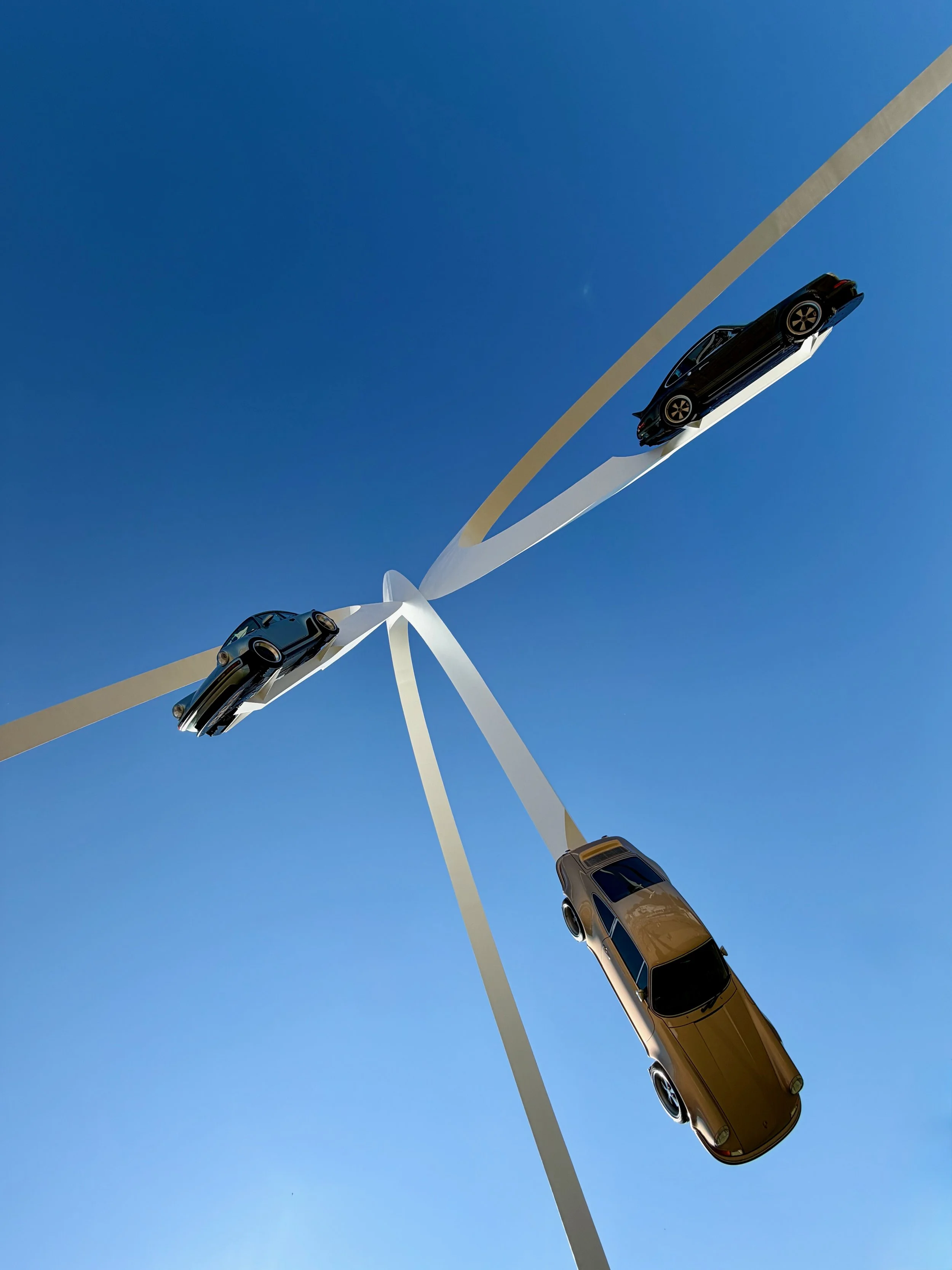 A Ferris wheel with car models attached to each spoke, viewed from below against a clear blue sky.