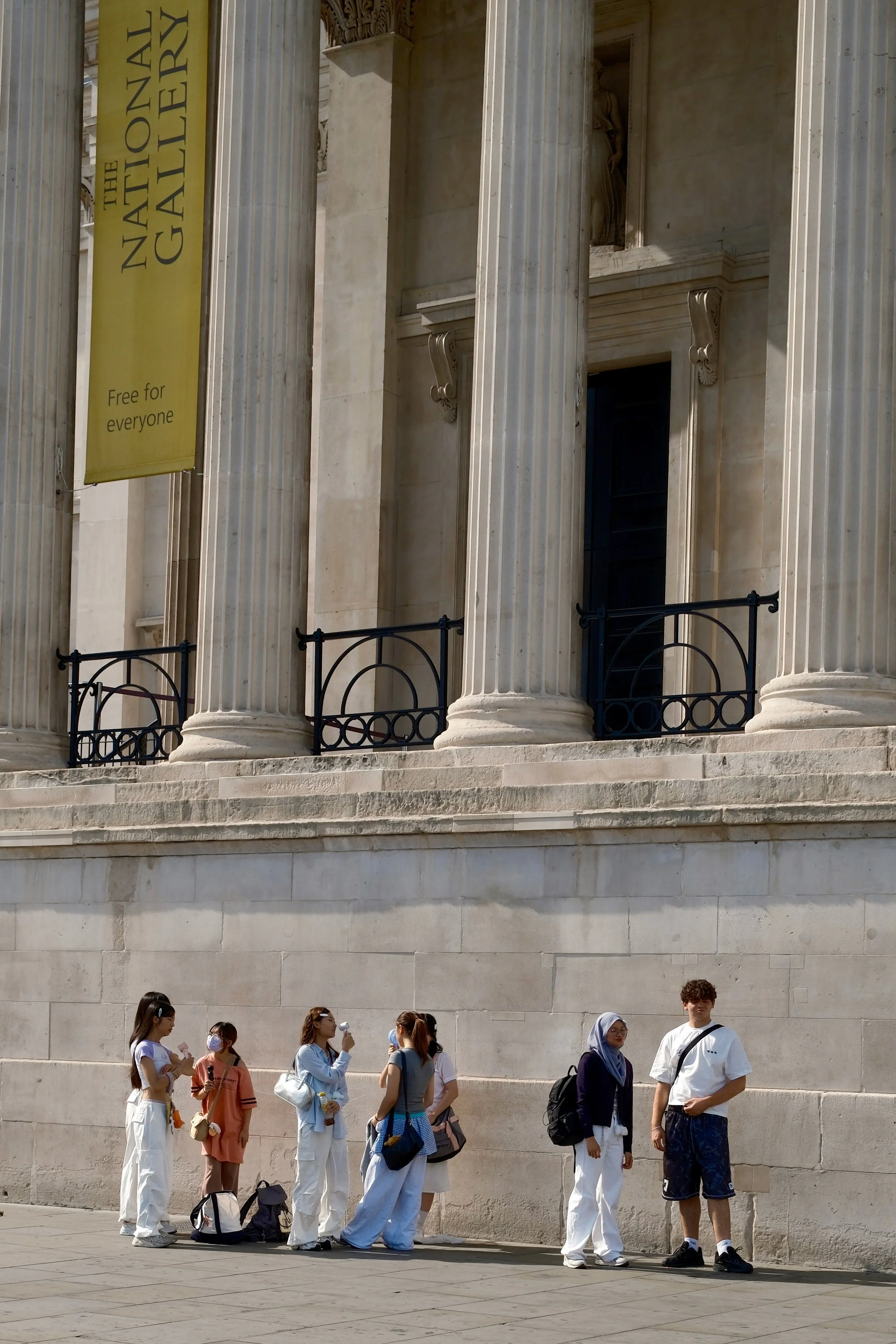 People standing in line outside The National Gallery, a building with tall classical columns and stairs.