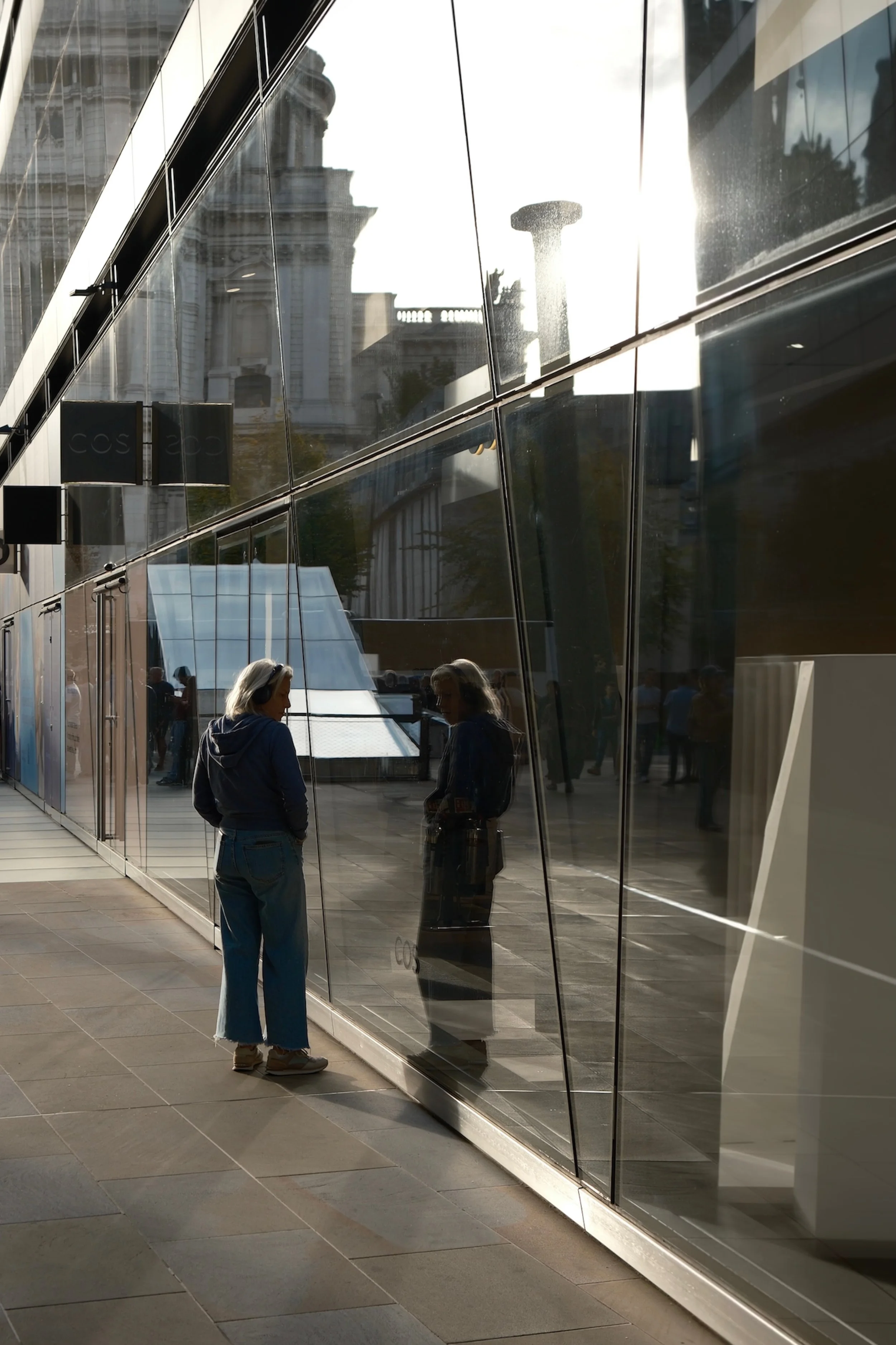 People reflected in a glass building with modern architecture in an urban area. Sunlight creates bright highlights and shadows.