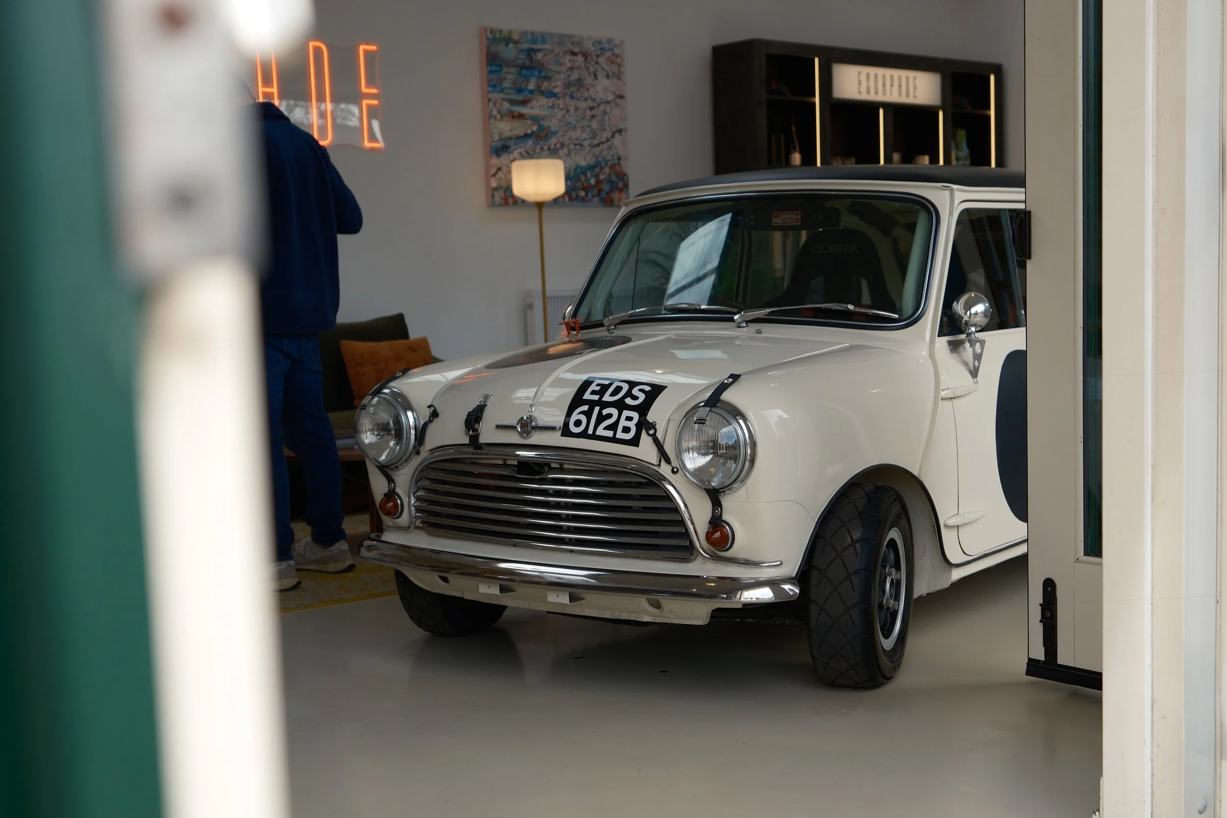A small white vintage car with the license plate 'EDS 612B' parked indoors, partially visible through an open door or window.