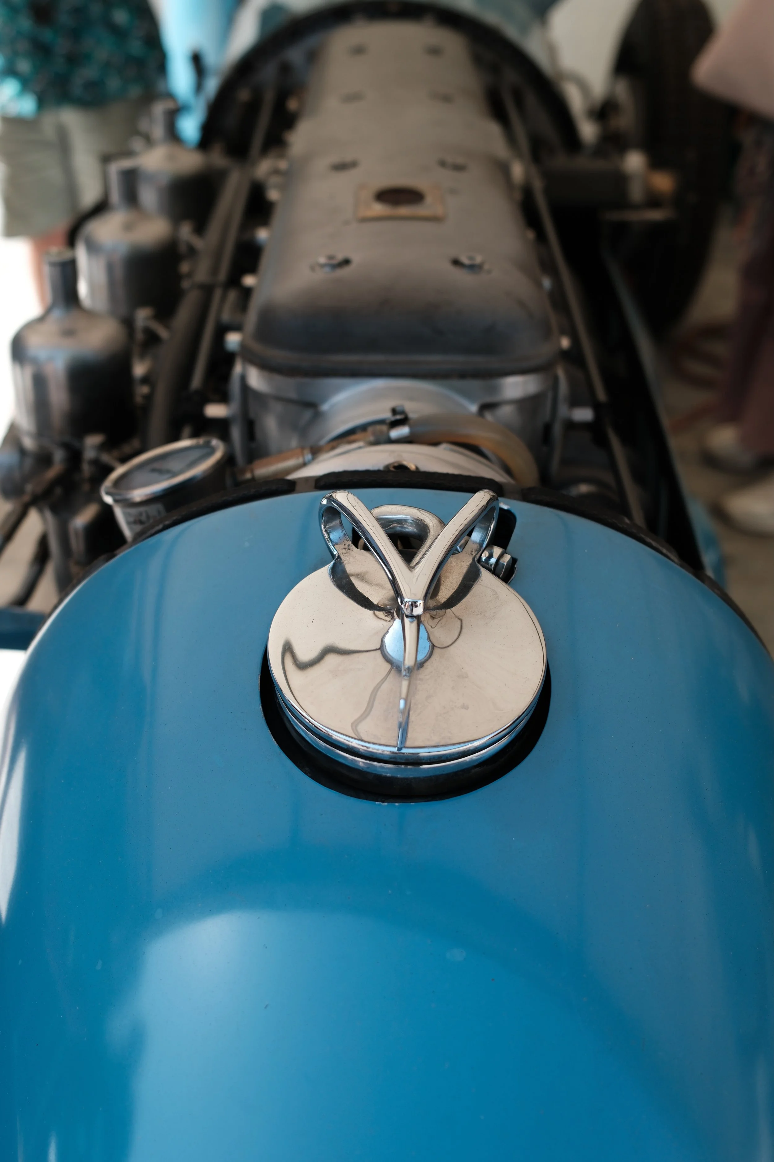 Close-up of a vintage blue car's front with a chrome emblem on the hood, showing the engine compartment.