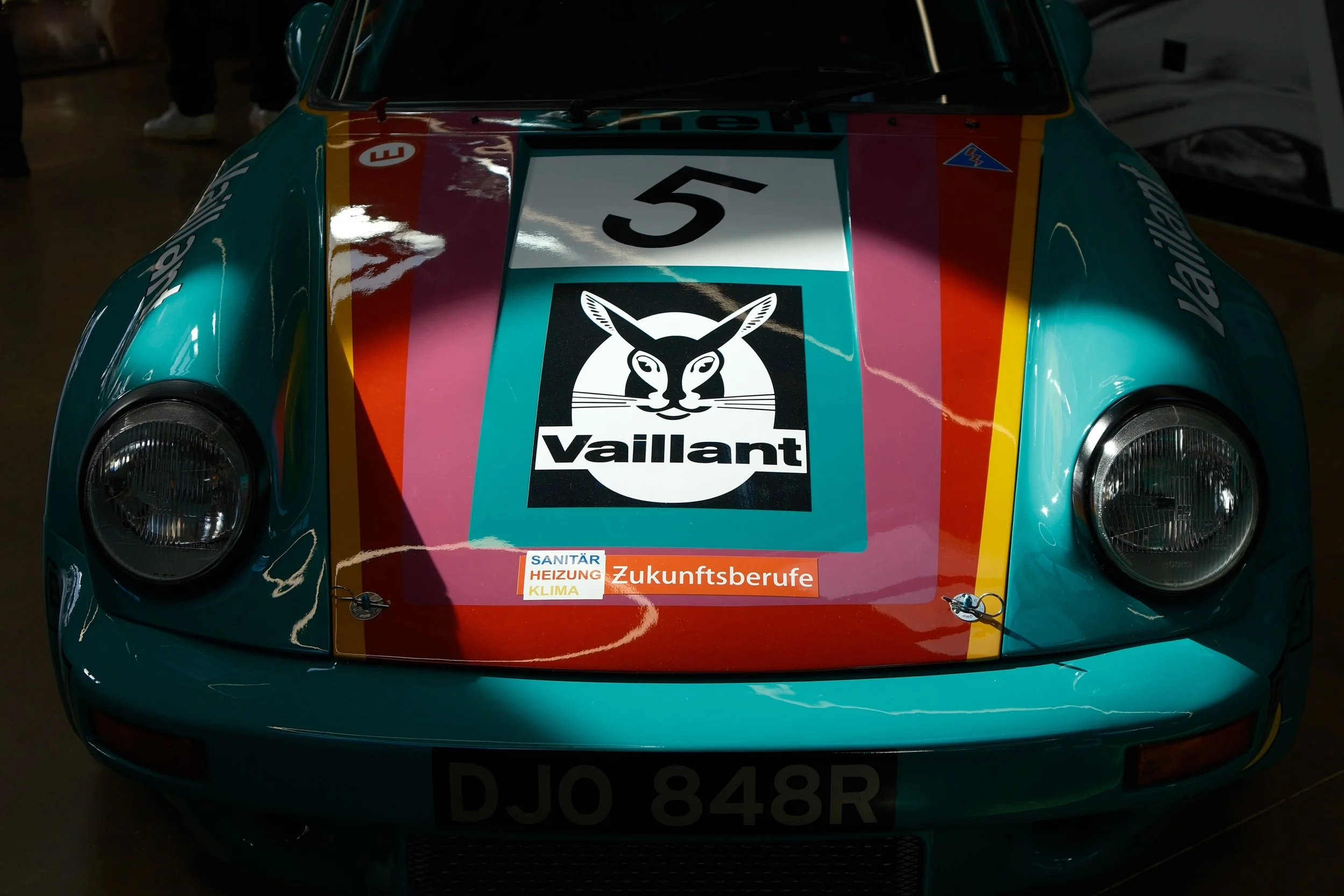 Close-up of a vintage race car's front with colorful racing stripes, race number 5, sponsor logos, and badges.