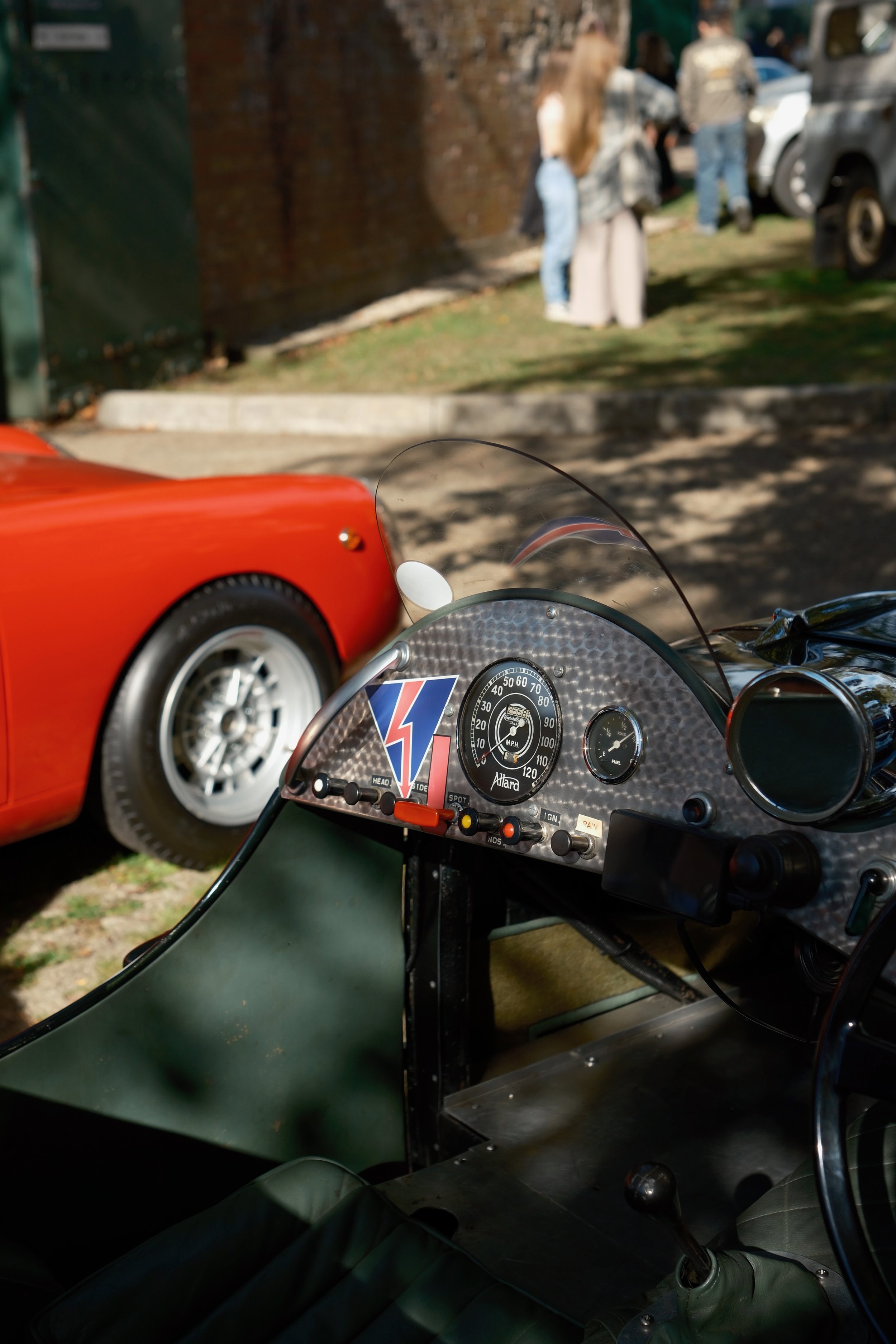 View from inside a vintage motorcycle looking out at a blurry street scene with people walking and parked cars in the background.