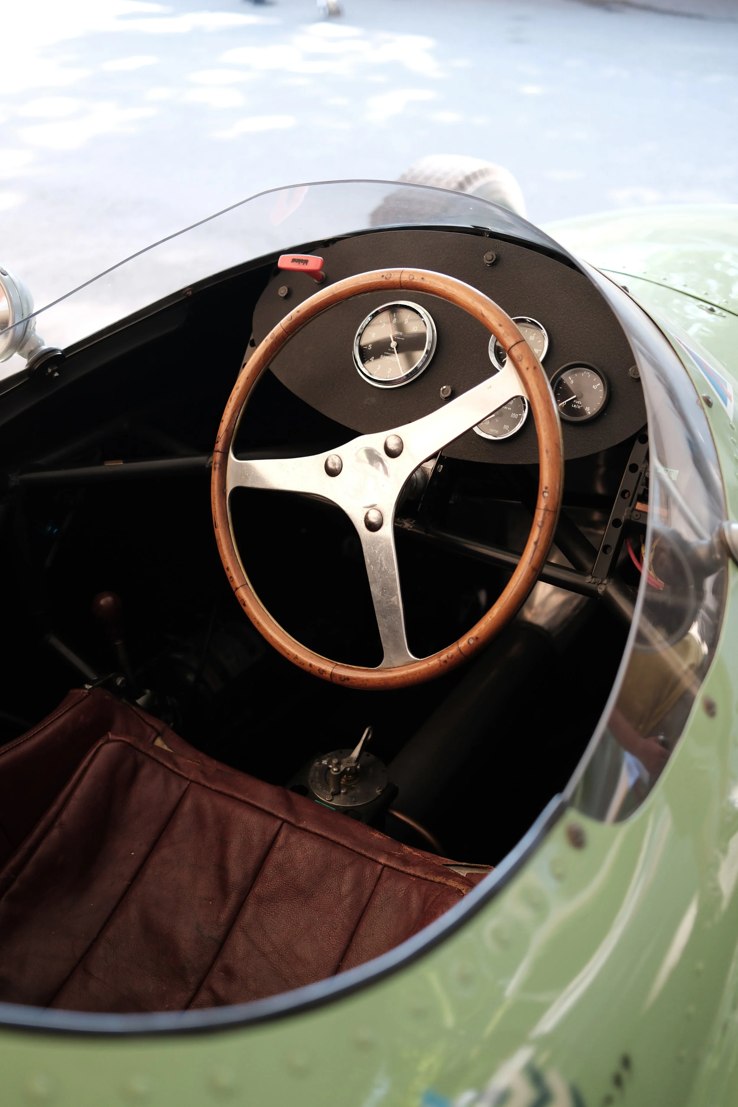 Interior view of a vintage car with a wooden steering wheel, analog gauges on the dashboard, and a leather seat.