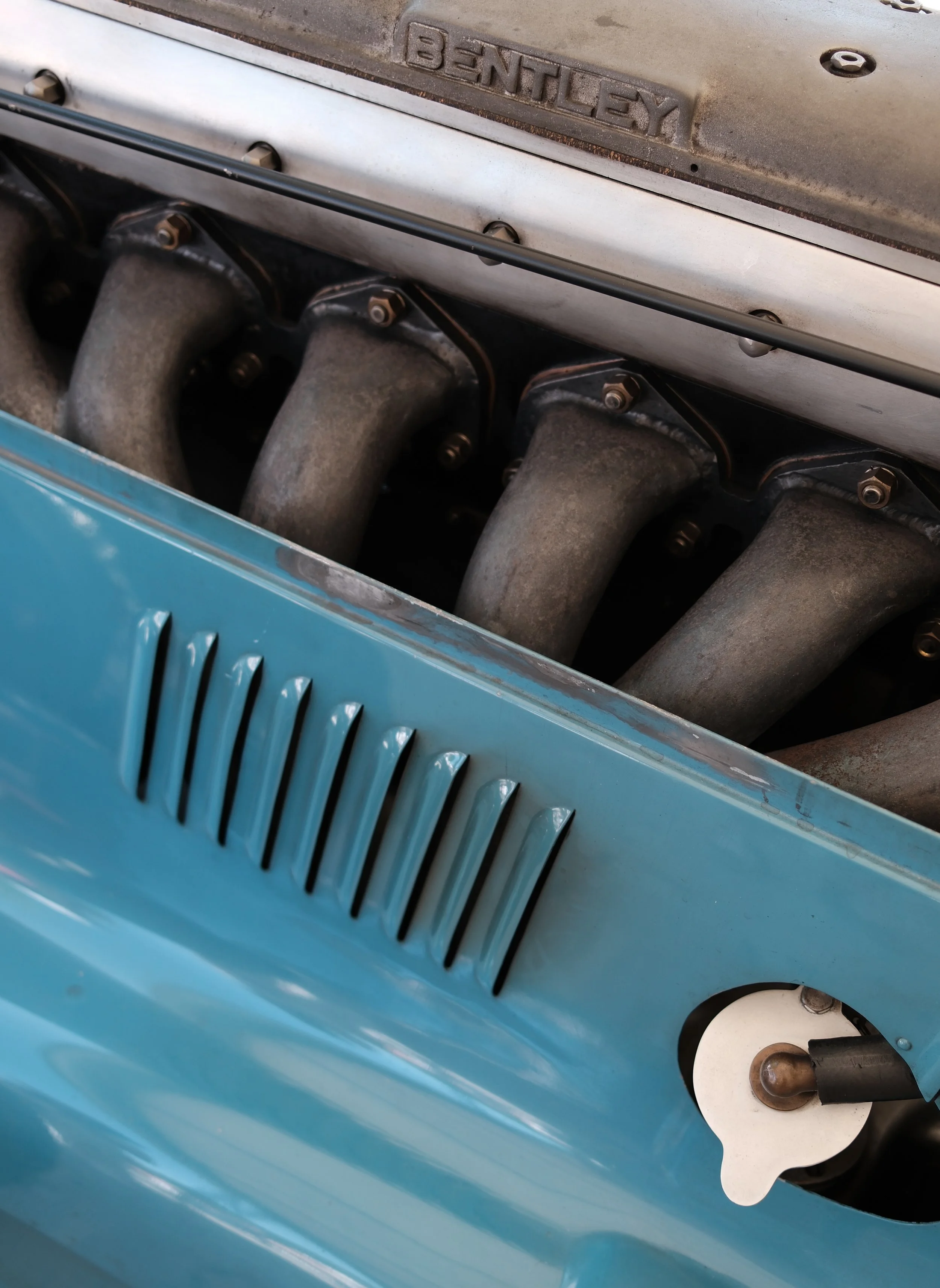 Close-up view of a vintage Bentley car engine with visible exhaust manifold and Bentley logo on top.