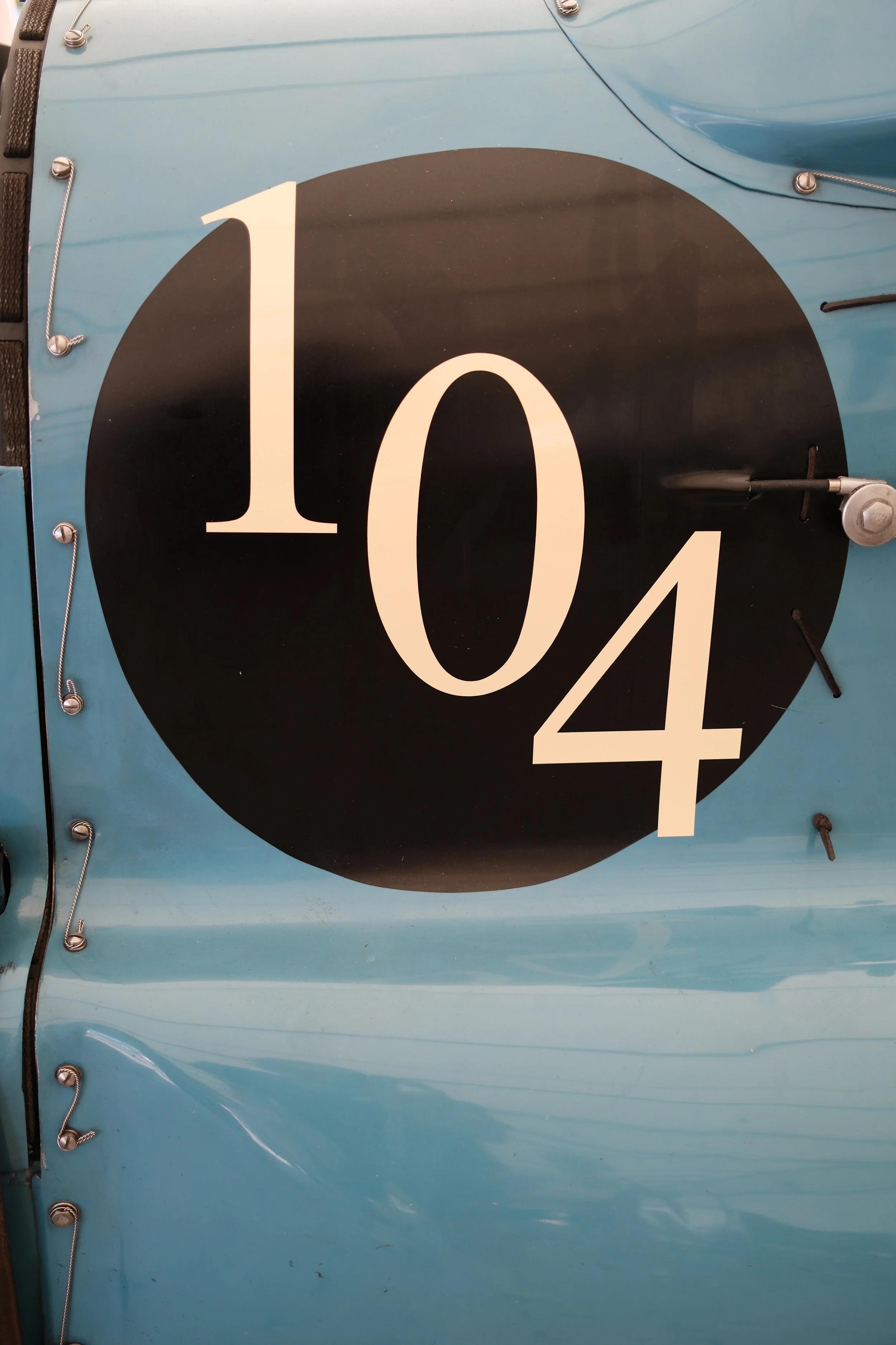 Close-up of vintage race car with large number '104' decal on blue body.