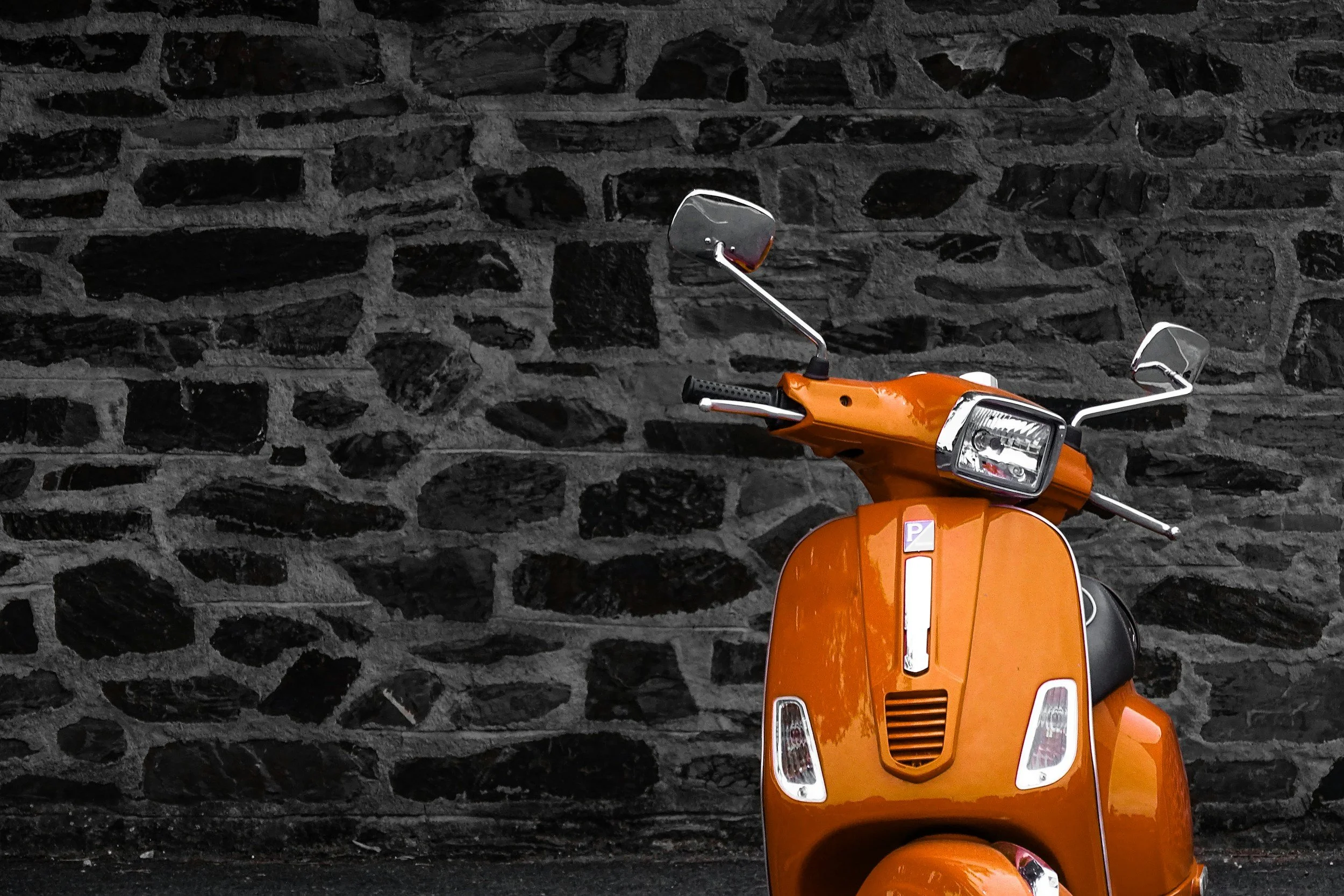 An orange vintage scooter parked in front of a textured black stone wall.