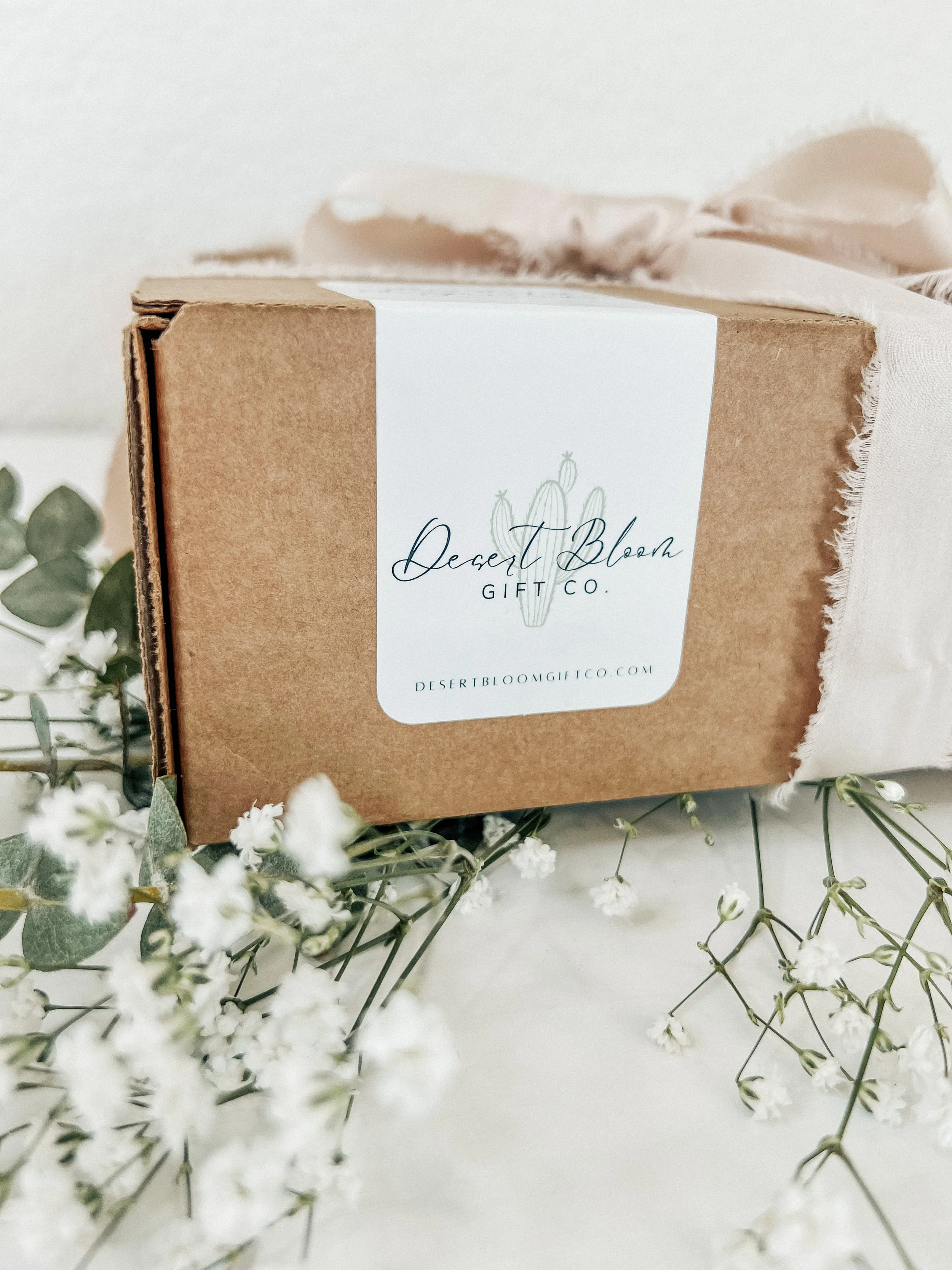 A cardboard box with a white label that reads 'Desert Bloom Gift Co.' surrounded by small white flowers and green leaves.