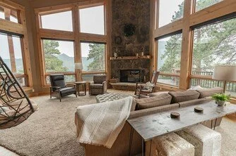 Spacious living room at Estes Park vacation home with large windows, stone fireplace, and cozy furniture