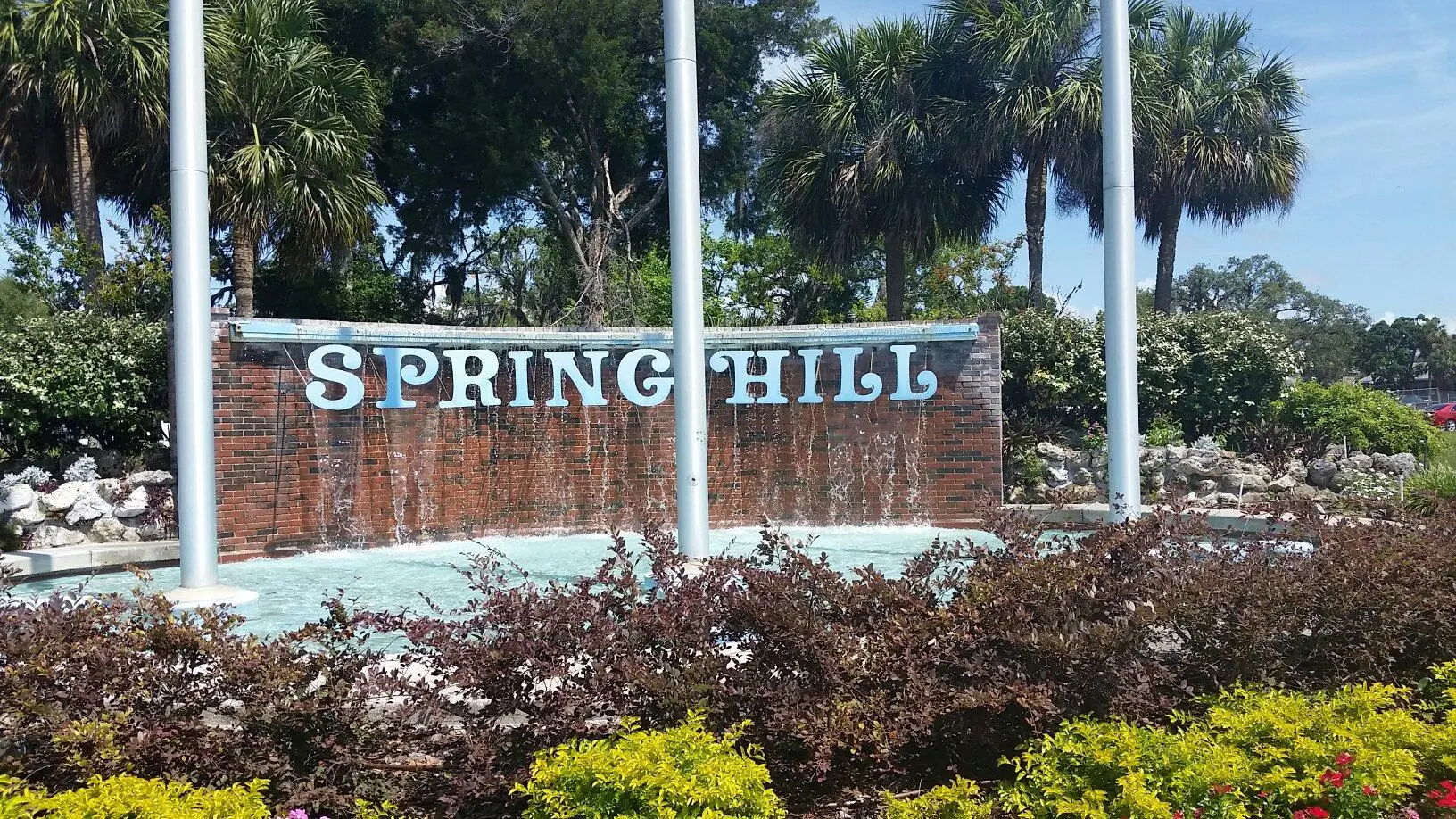 Spring Hill sign with water feature and tropical trees in the background, surrounded by colorful landscaping.