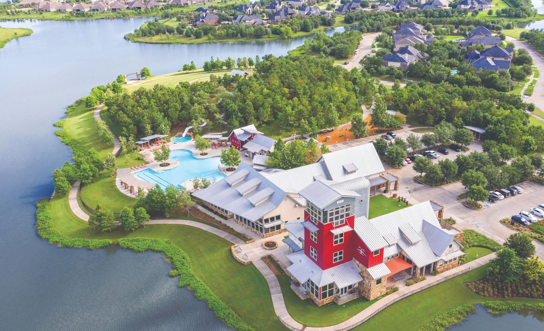 Aerial view of a lakeside community with a modern building, swimming pool, and green landscaping.