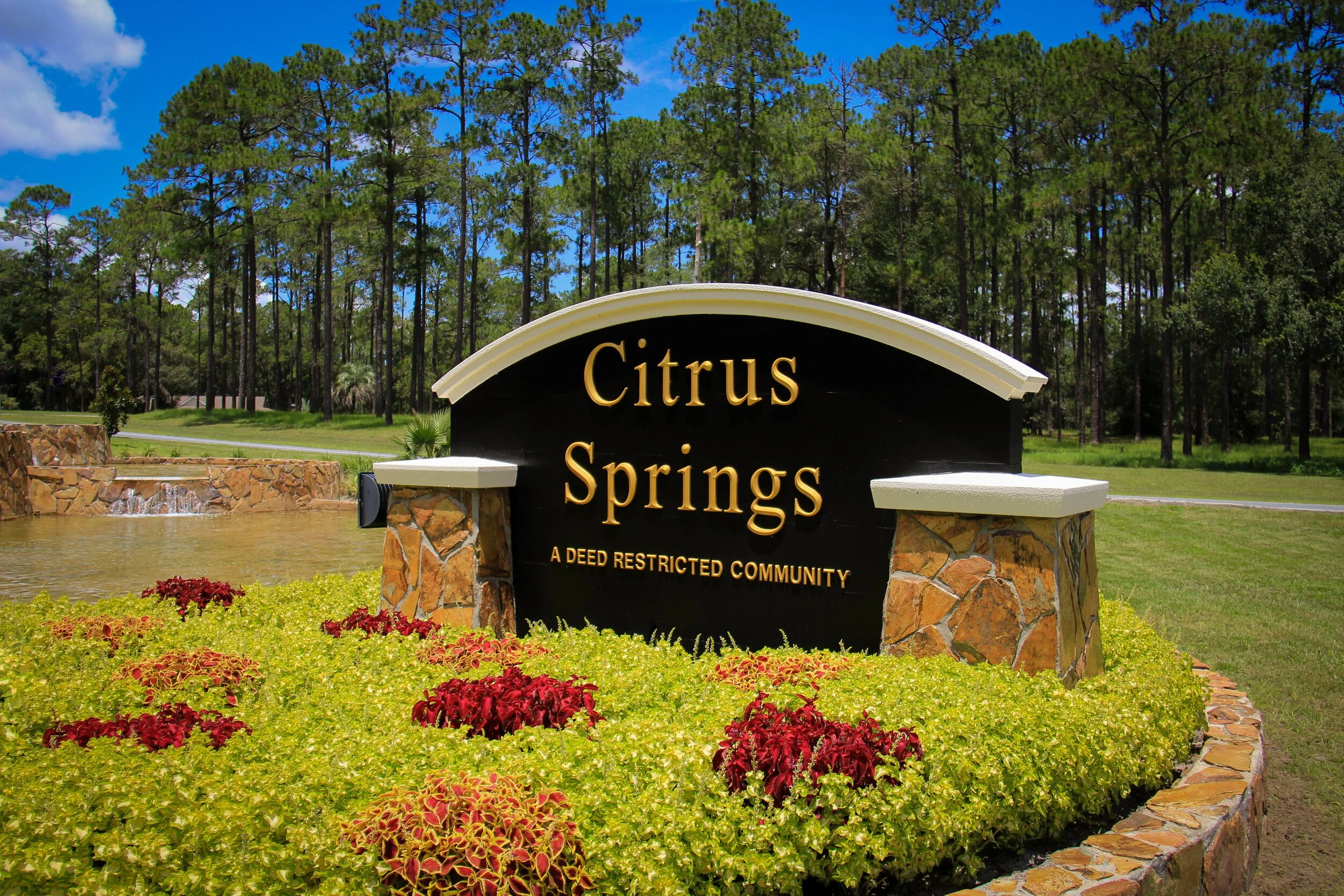 Entrance sign for Citrus Springs, a deed restricted community, with a landscaped garden and trees in the background.
