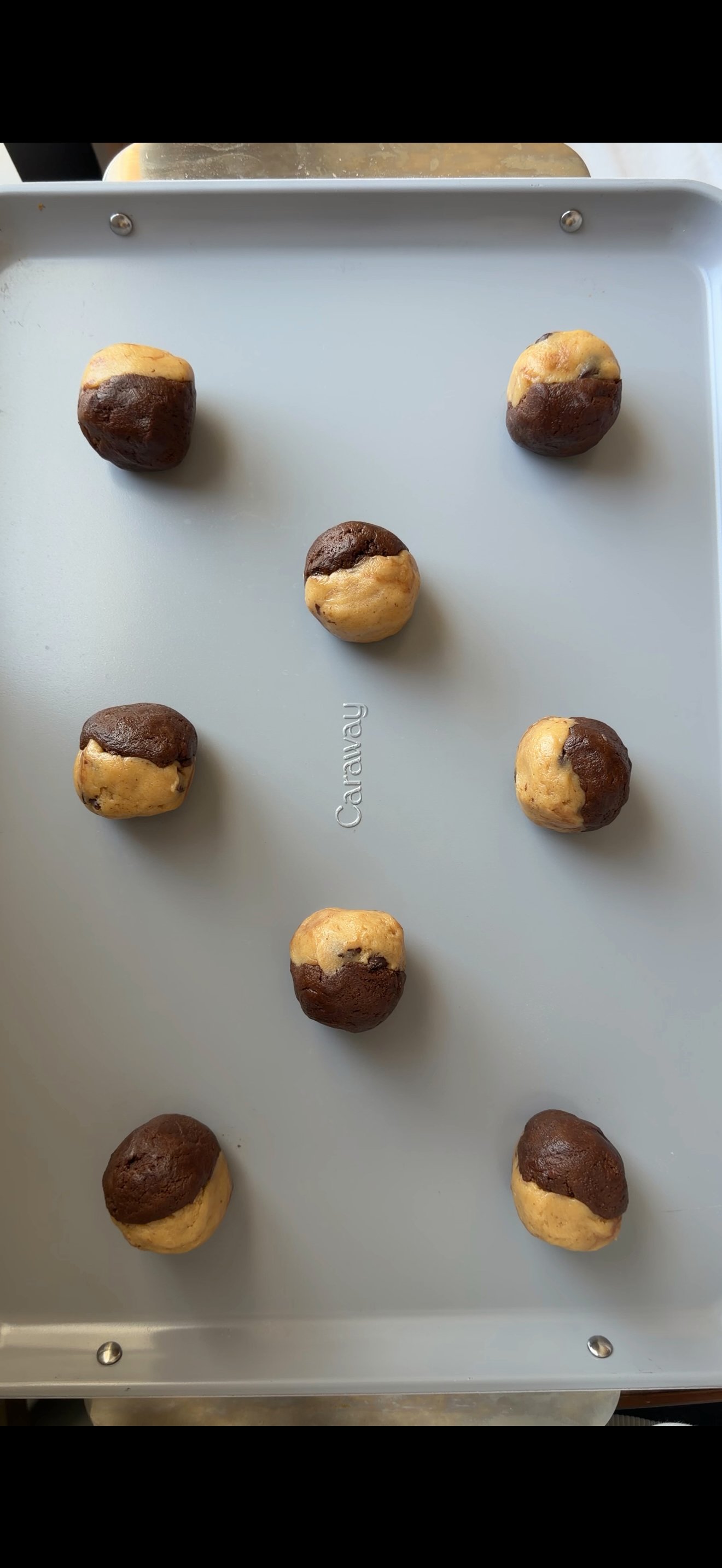 Rounded scoops of brookie dough spaced on a baking tray, chocolate chunks visible, ready to go into the oven.