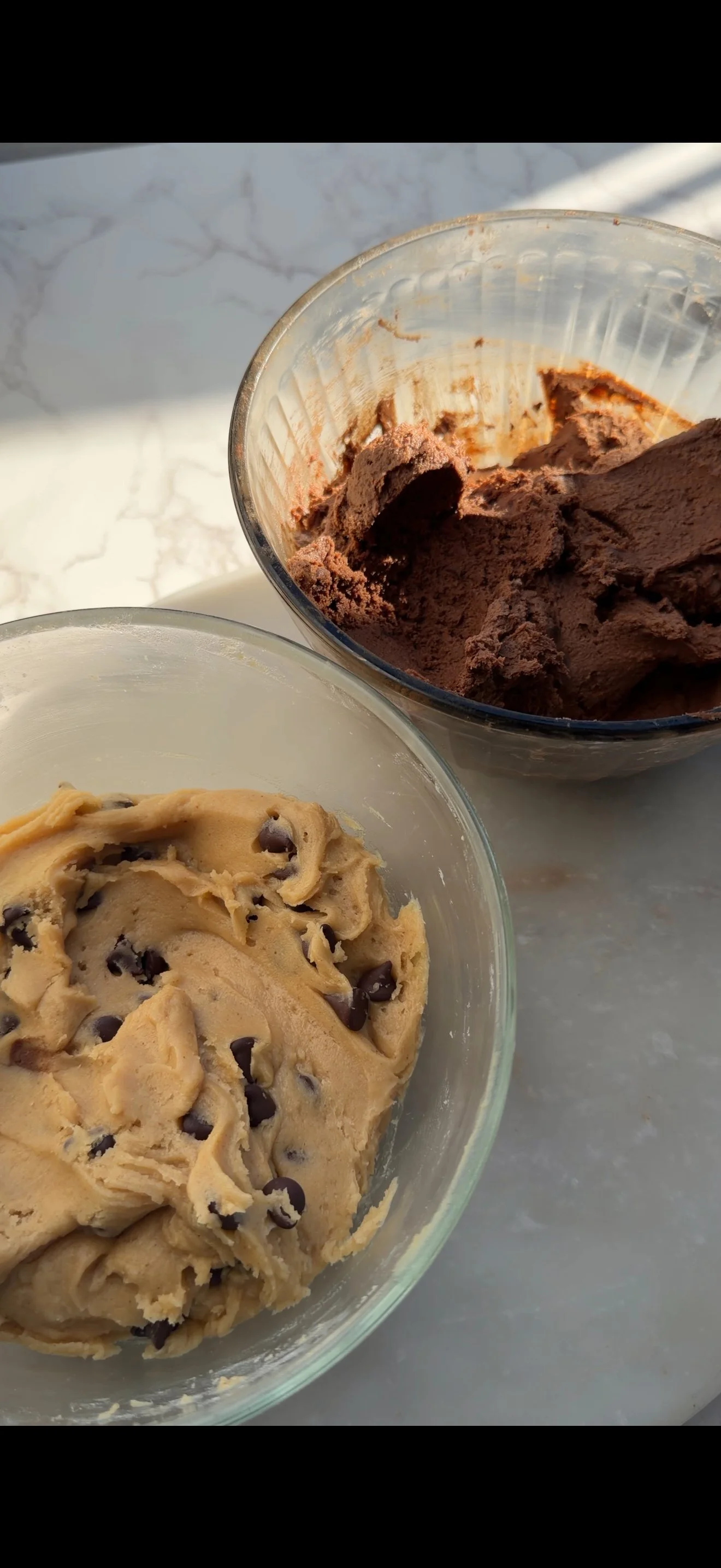 Close up of thick chocolate chip cookie dough and dark fudgy brownie batter in separate bowls before combining for brookie cookies.