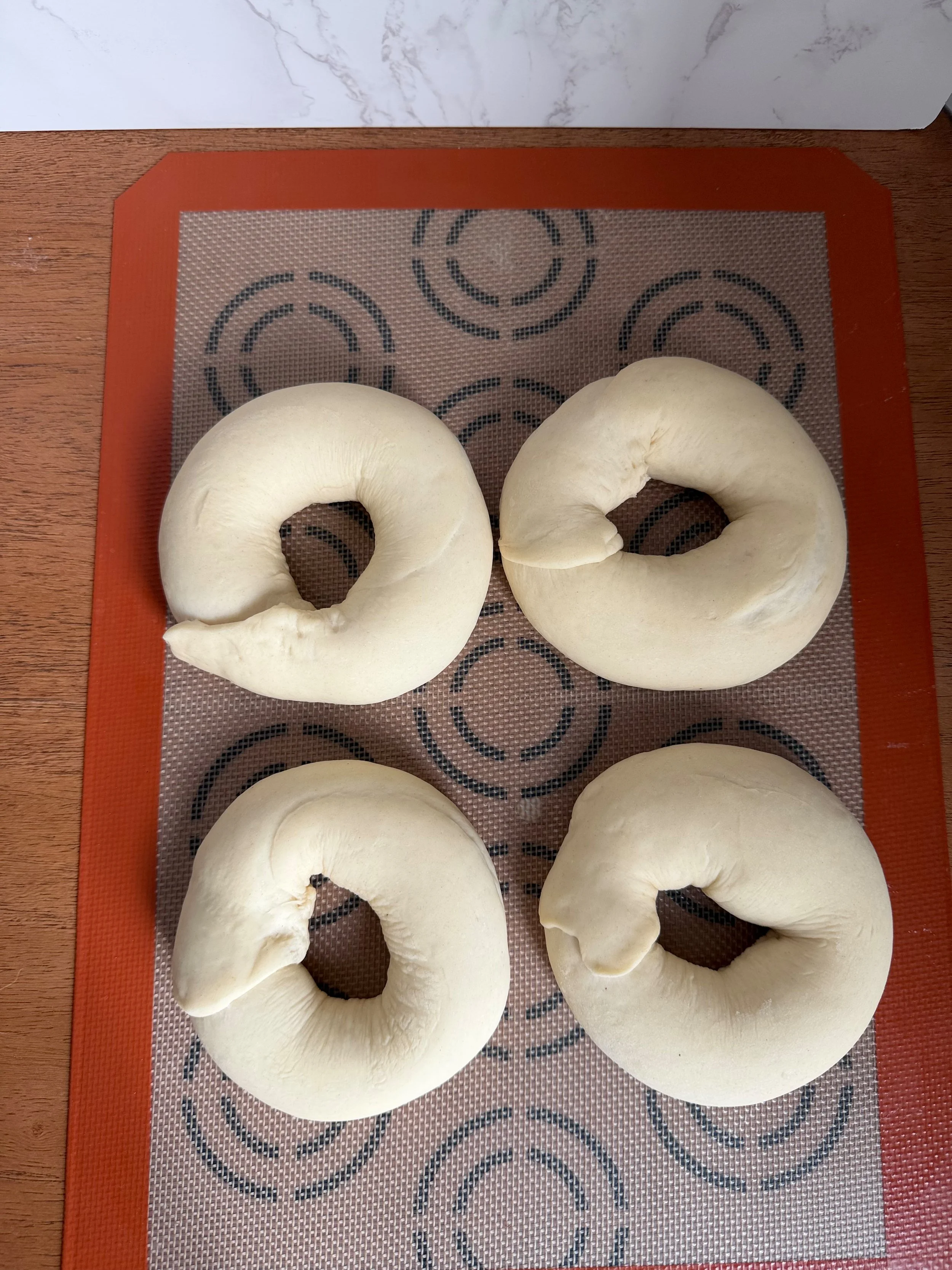 shaped bagel doughs on a baking sheet rising