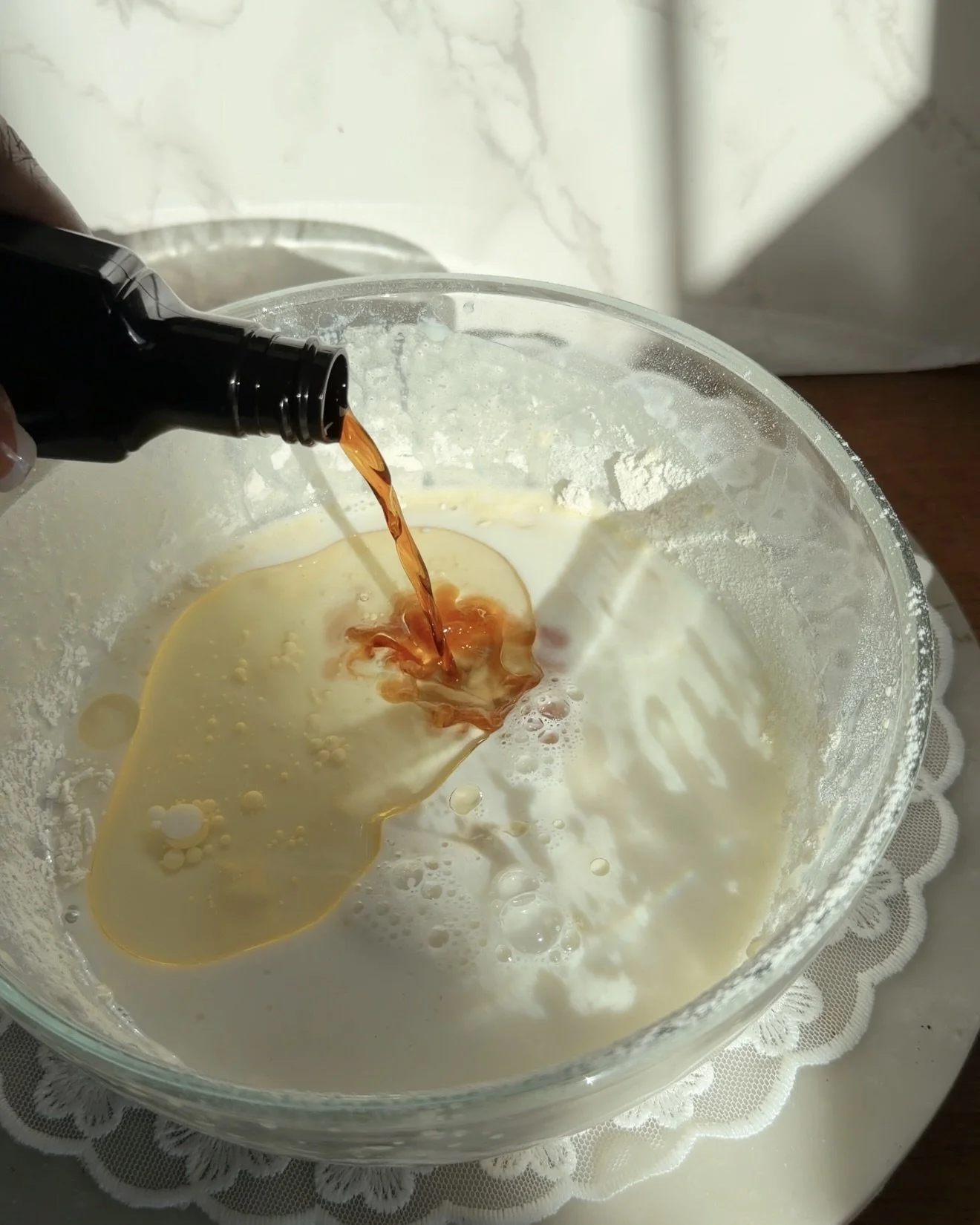 vanilla extract being poured into glass mixing bowl with cake batter