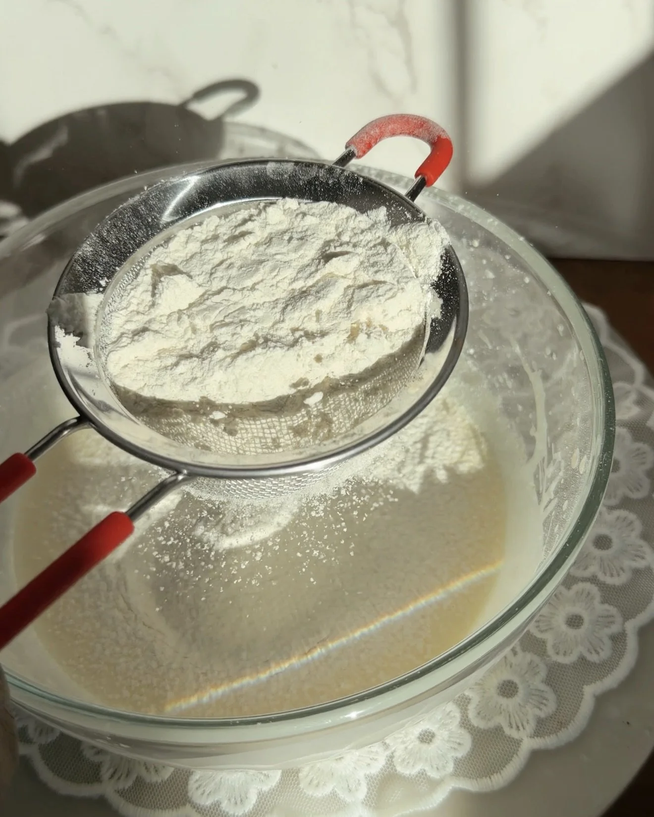 flour, baking powder, and salt being sifted into glass mixing bowl with cake batter