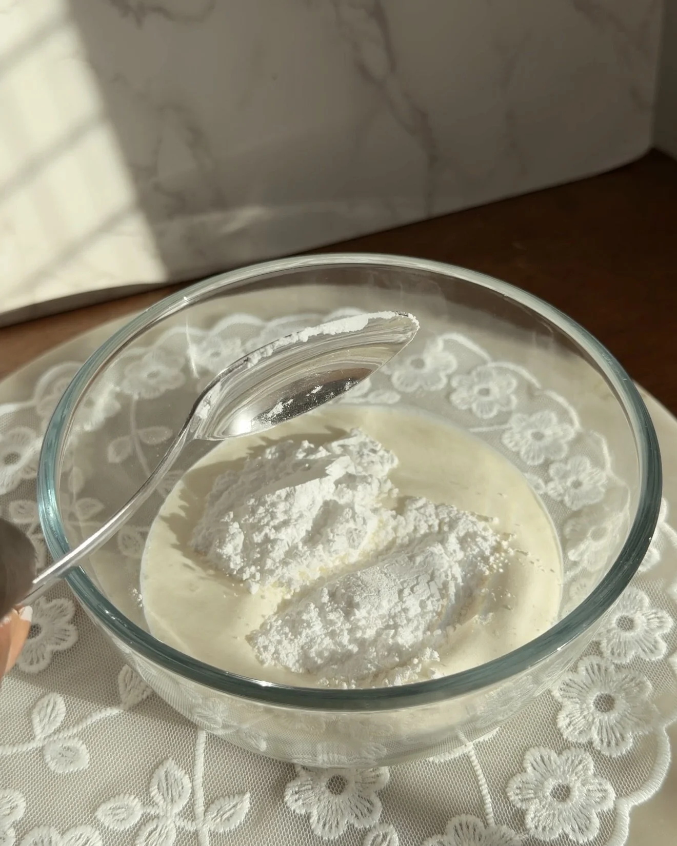 powdered sugar being added to heavy cream in glass mixing bowl to make whipped cream