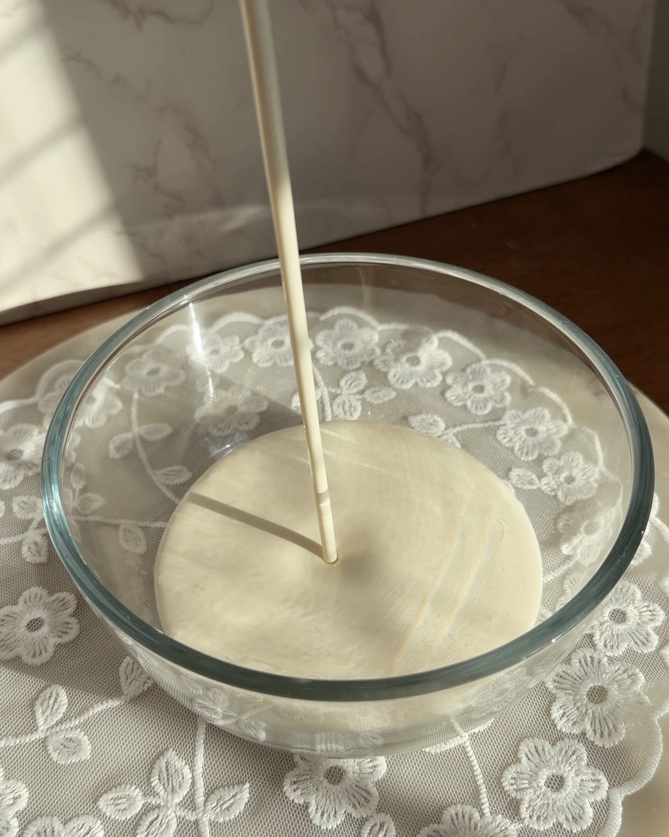 cold heavy whipping cream being poured into glass mixing bowl to make whipped cream
