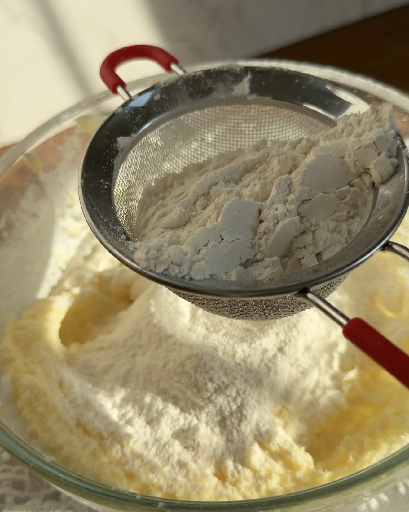 Flour being sifted into wet ingredients on the counter