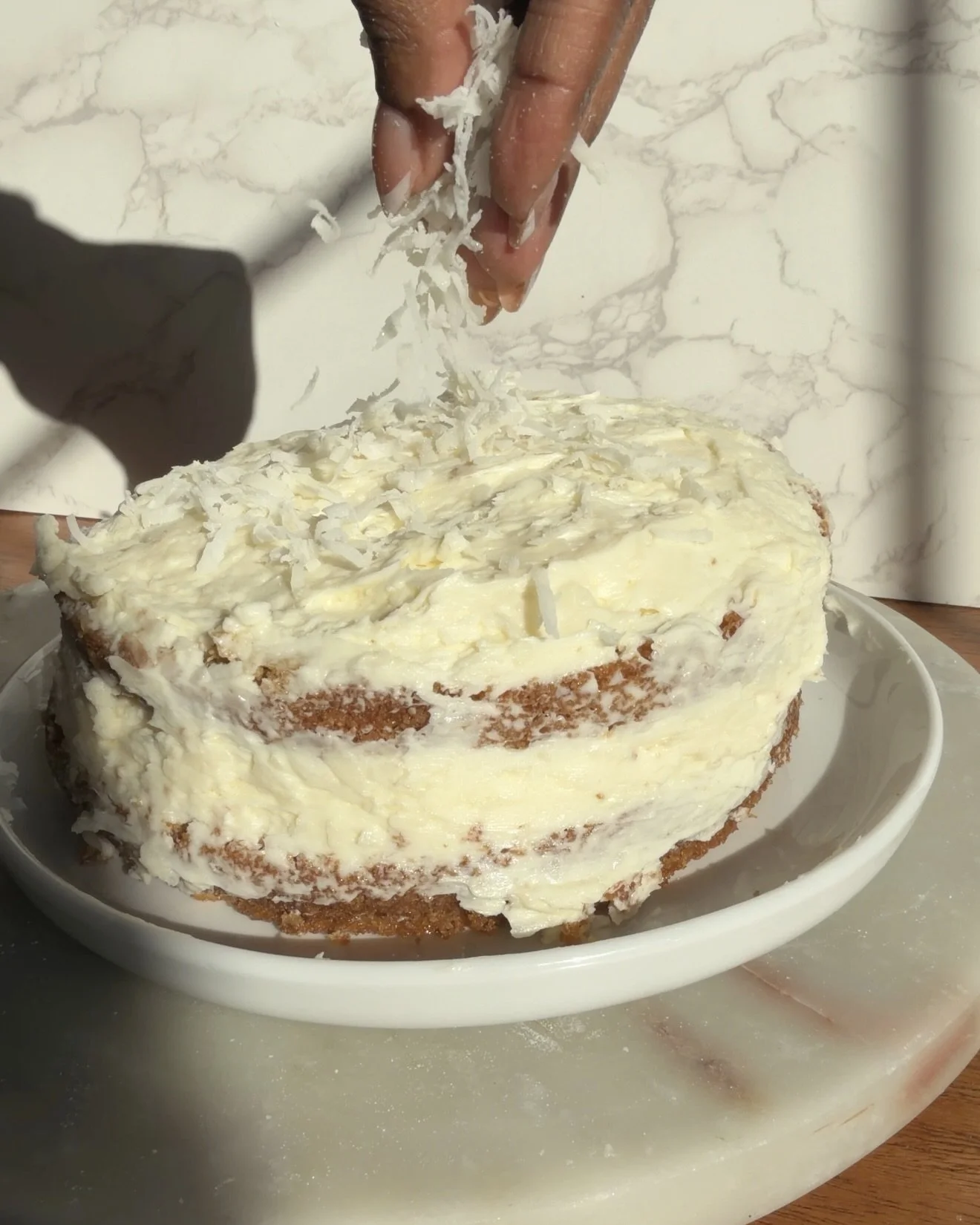 Fully frosted cake being covered in coconut flakes