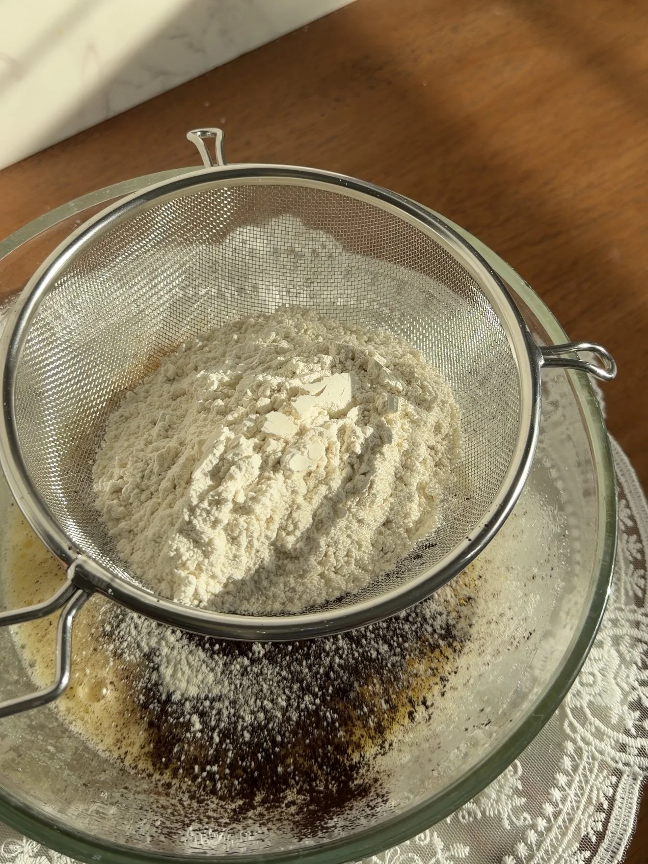 Flour being sifted into glass mixing bowl on the counter.