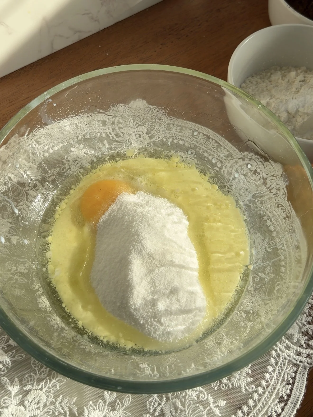 Glass mixing bowl on the counter with milk, oil, sugar, and egg. 