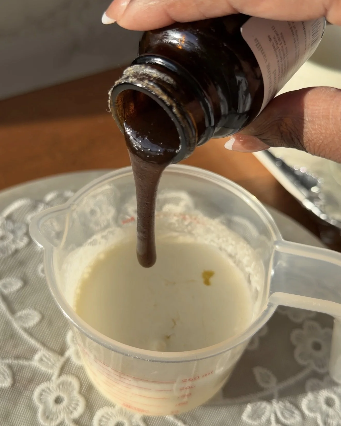 Plastic measuring cup on countertop with heavy cream, egg, and vanilla bean paste. 