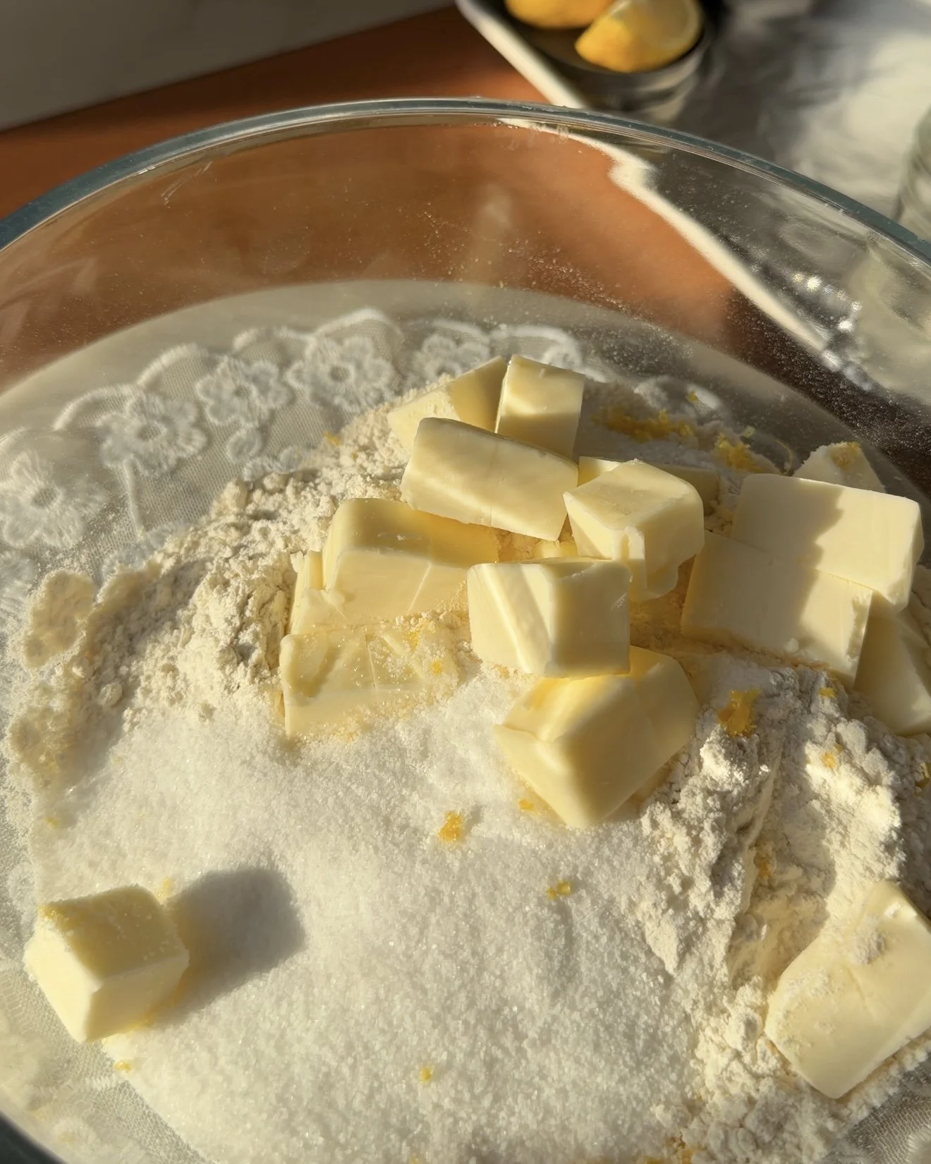 Glass mixing bowl on countertop with dry ingredients and frozen cubes of butter