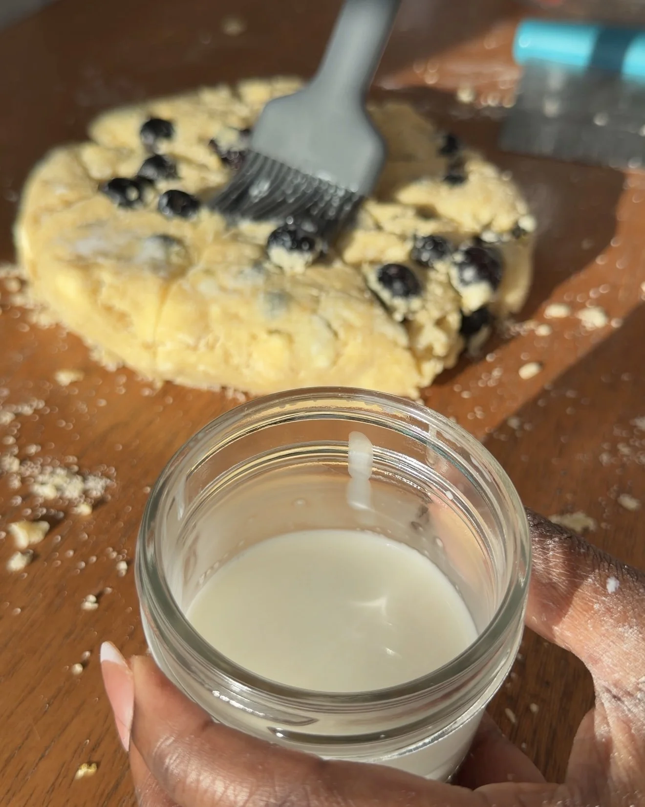 Cream and water mixture being brushed on top of scone dough disk. 