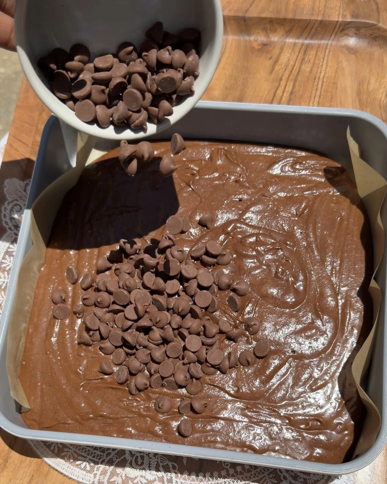 Chocolate chips sprinkled on top of brownie batter in brownie pan. 