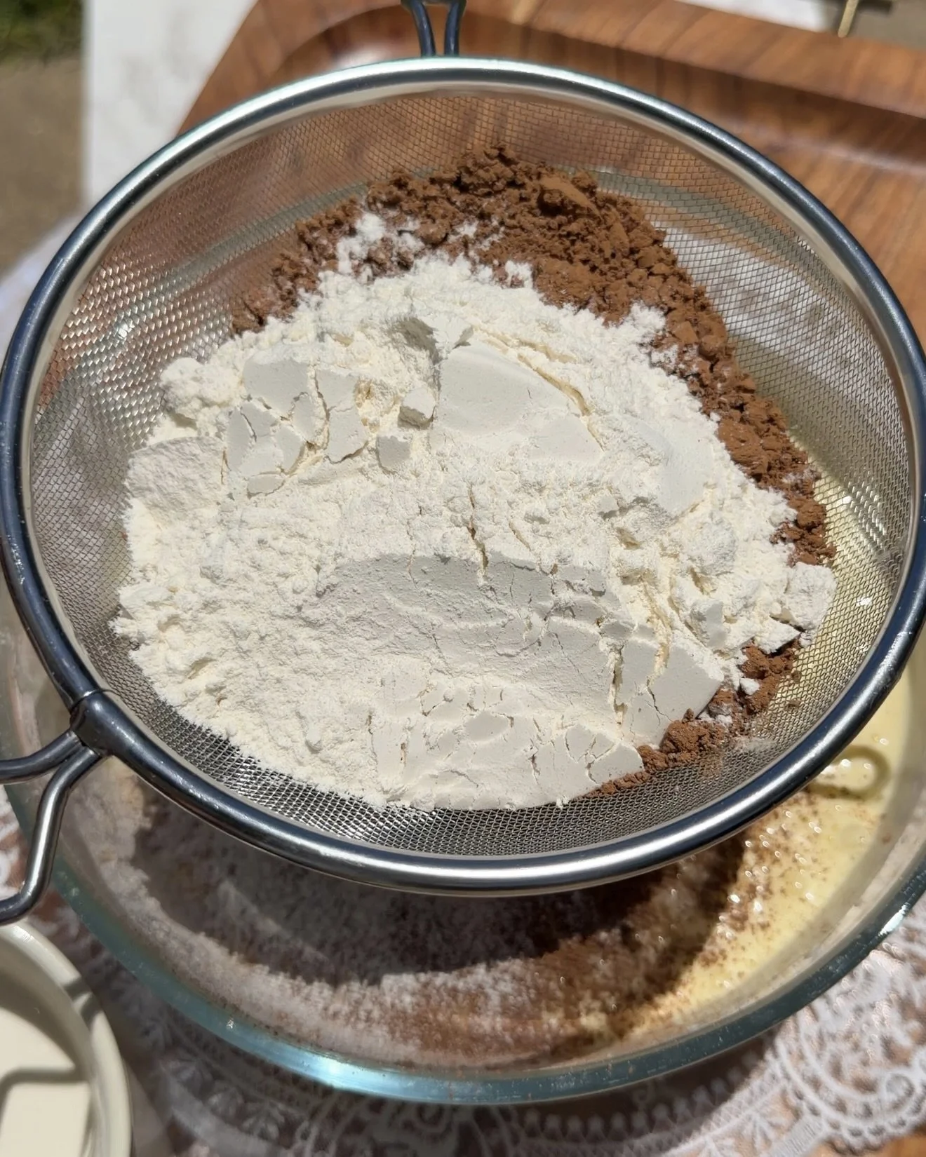 Flour and cocoa powder being sifted into wet ingredients in mixing bowl.