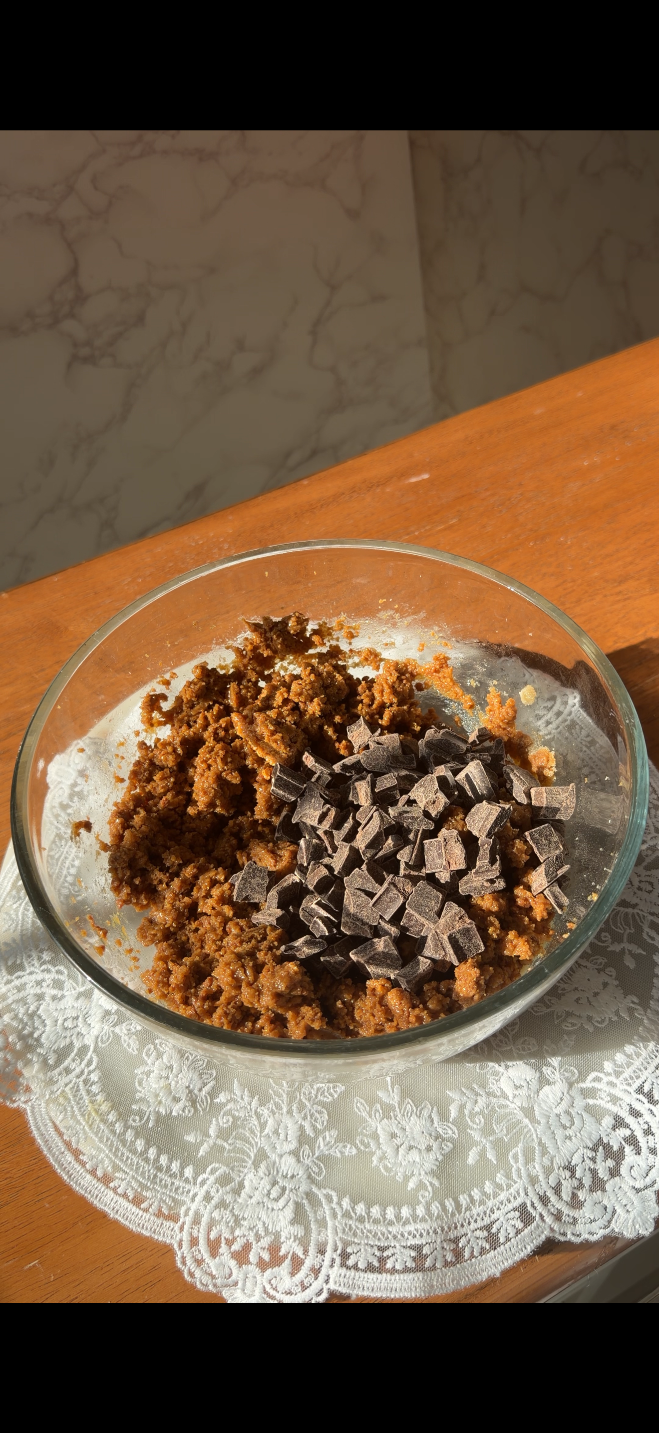 Glass mixing bowl with cookie dough and chocolate chips on top on counter. 