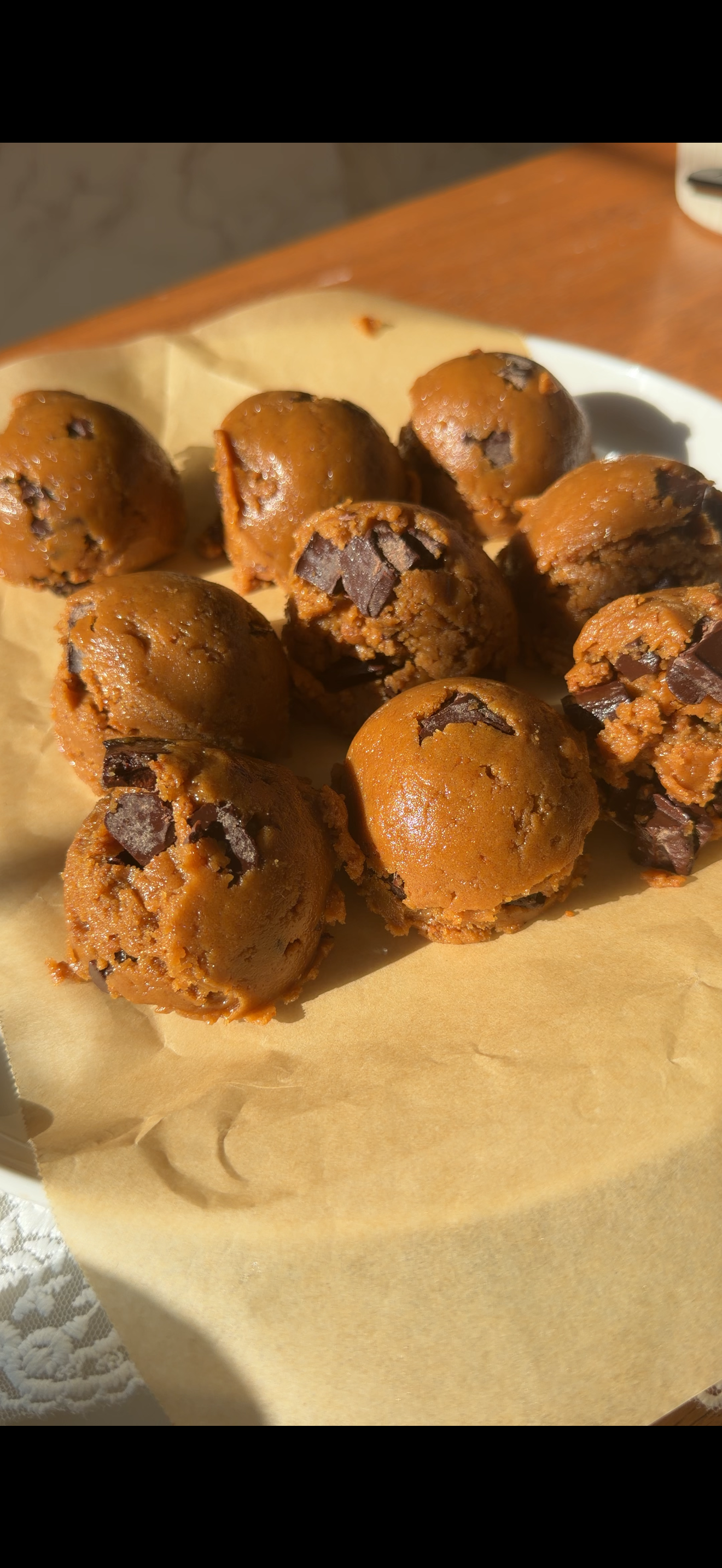 9 cookie dough scoops on a plate lined with parchment paper on the counter. 