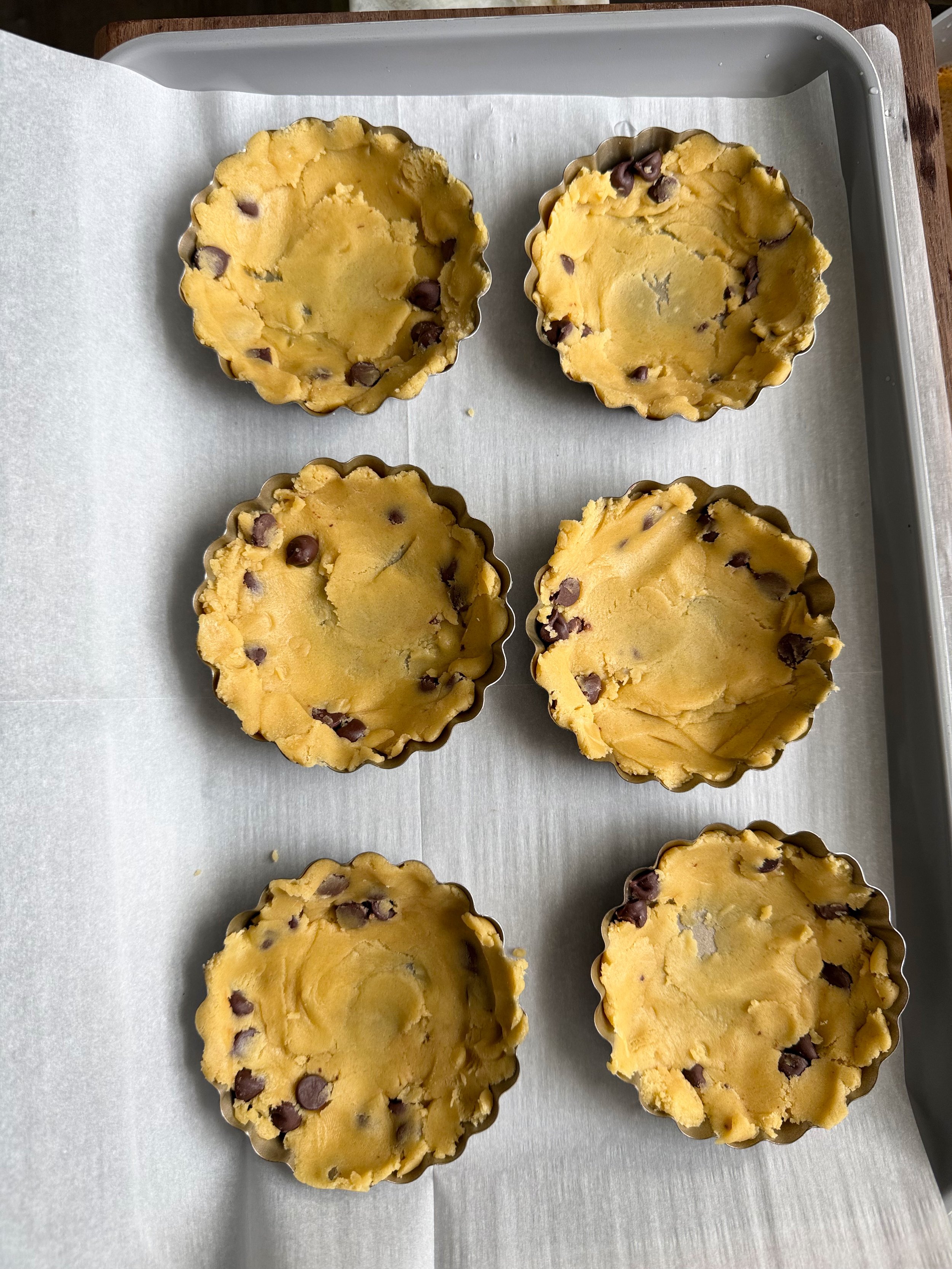 Six tart pans on the counter with cookie dough spread evenly in tarts. 